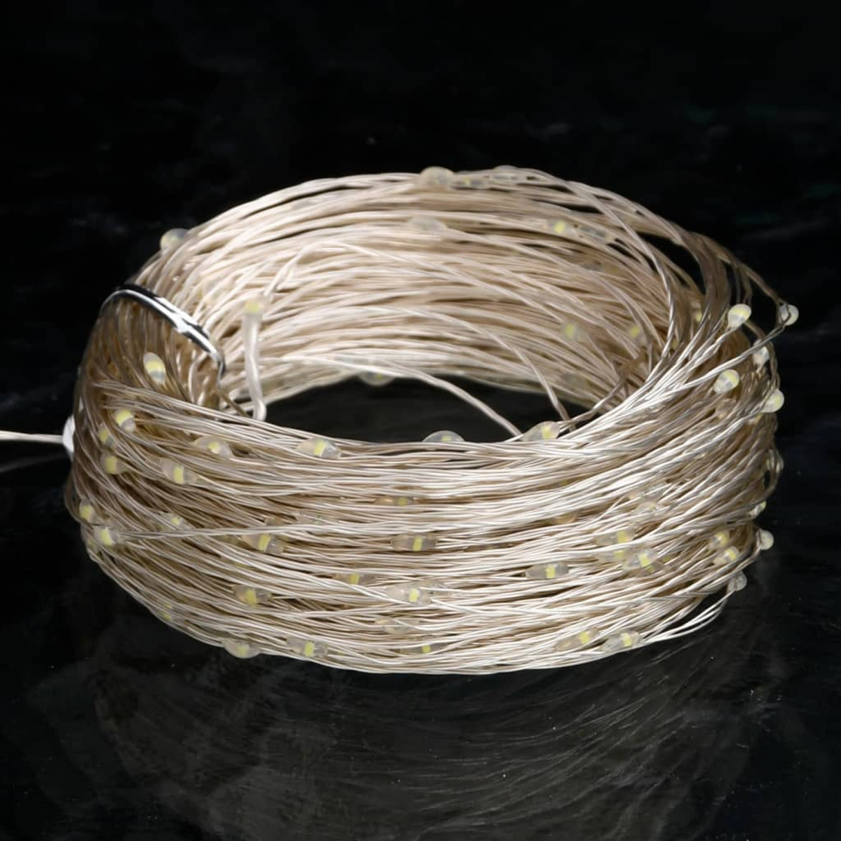 Aufgerollte Lichterketten mit vielen kleinen, runden, gelben Lichtern. Die Lichter liegen auf dunkler, reflektierender Oberfläche.