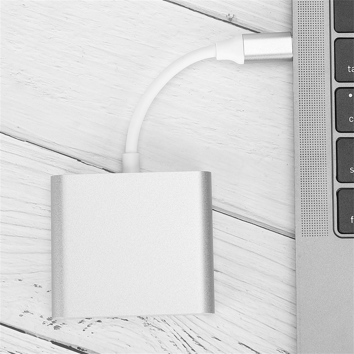 Ein silberner Adapter, der mit einem Laptop verbunden ist. Ein weißes Kabel ist ebenfalls sichtbar.