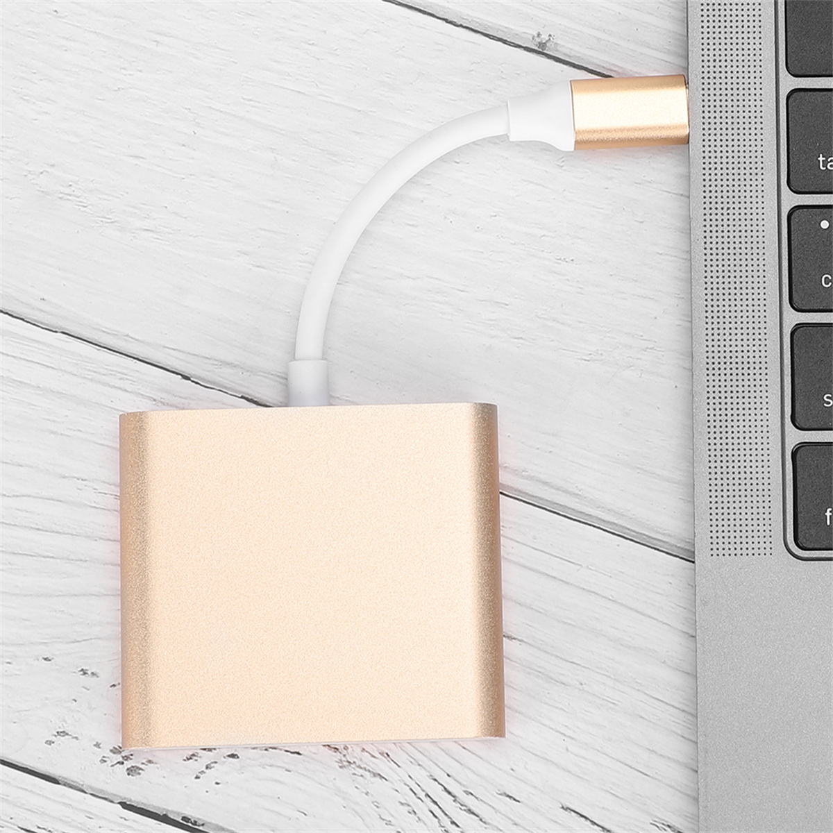 Ein goldener Adapter ist an einen Laptop angeschlossen. Die Laptop-Tastatur befindet sich auf der rechten Seite, auf einer Holzoberfläche.