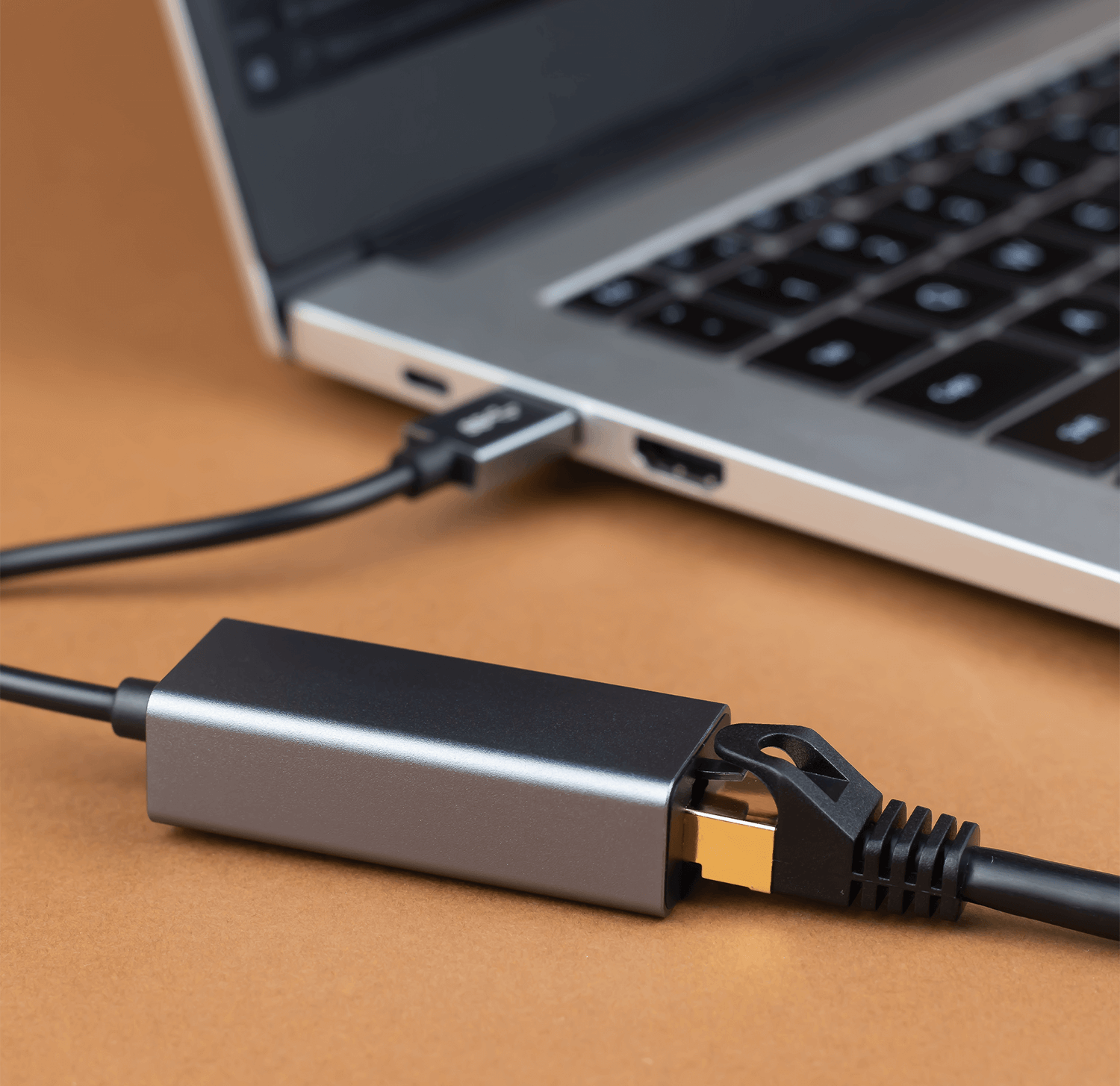 Laptop podłączony do adaptera i czarnego kabla, na brązowej powierzchni.