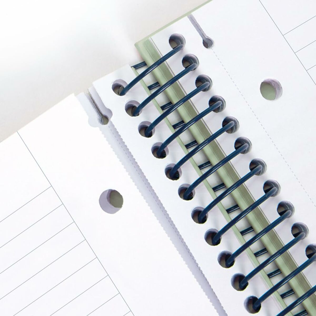 Zbliżenie na spiralny notatnik z zielonym grzbietem i papierem w linie, otwarty na białej powierzchni.