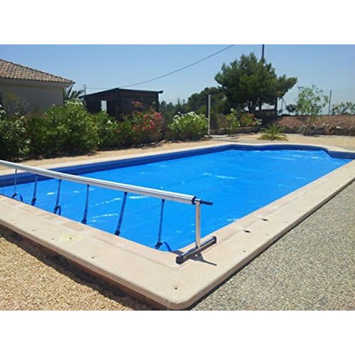 Blauer Swimmingpool mit blauer Abdeckung. Der Pool befindet sich in einem Garten mit Pflanzen und Haus im Hintergrund.