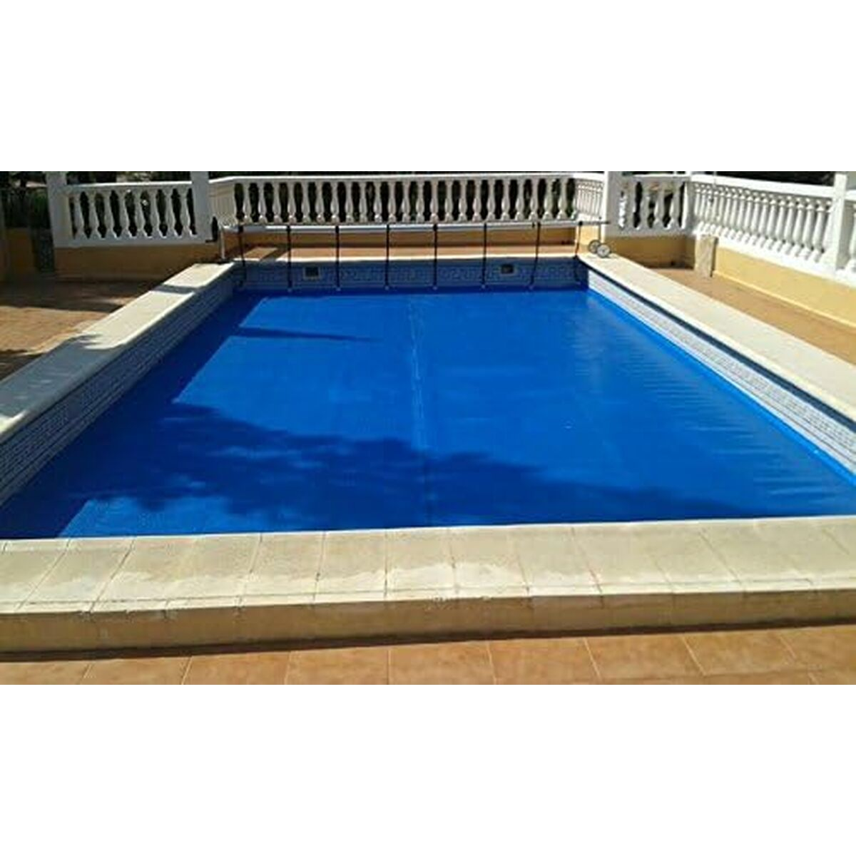 Blau abgedecktes Schwimmbecken mit weißen Geländern an einem sonnigen Tag.