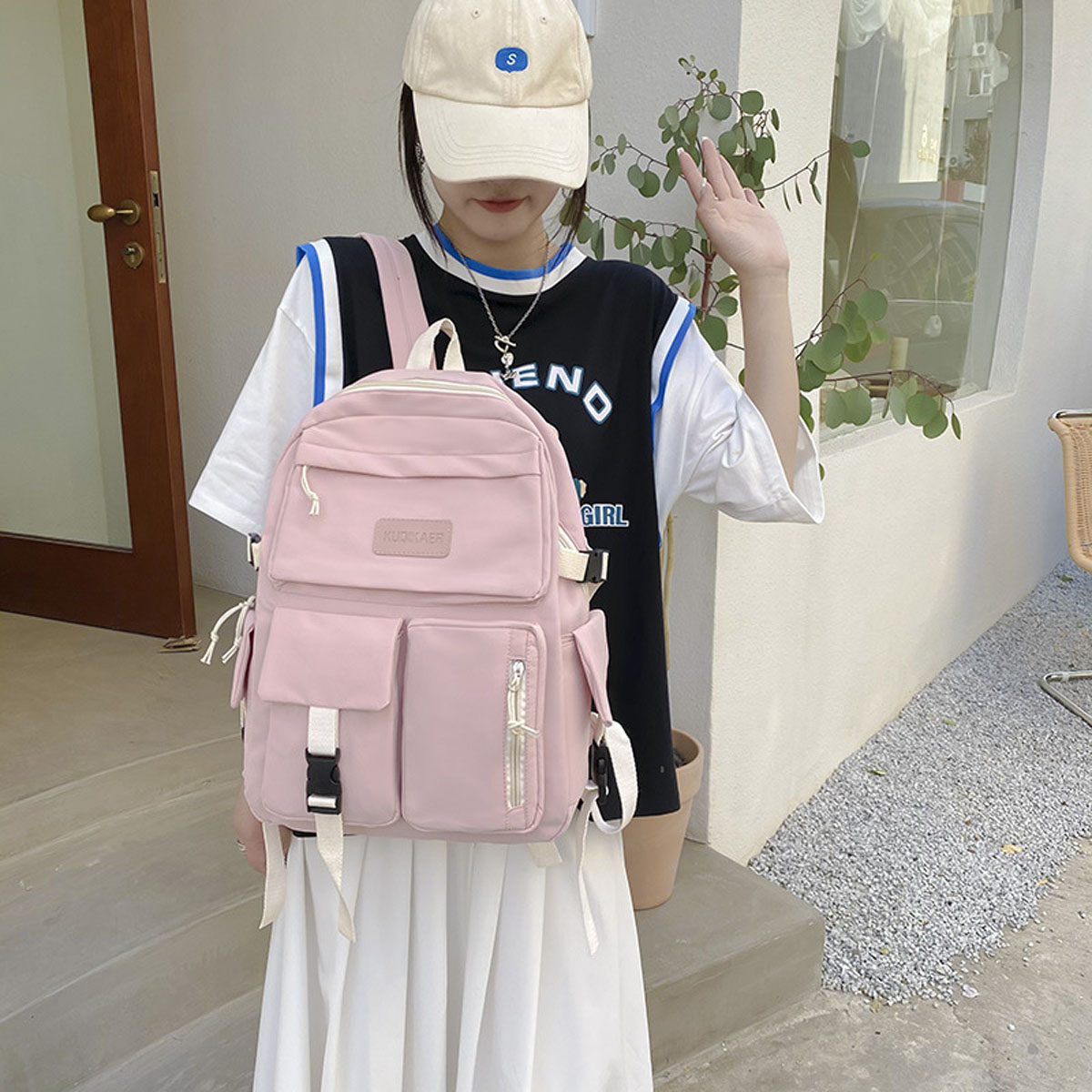 Frau mit Rucksack, weißem Rock, schwarzem Oberteil und Baseballkappe. Pinker Rucksack mit Taschen, weißen Trägern und Reißverschluss.