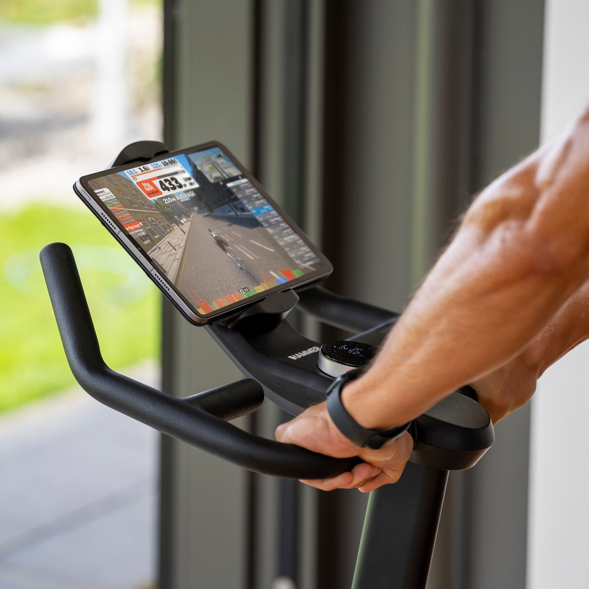 Une personne utilise un vélo d'exercice avec une tablette affichant un jeu de simulation cycliste.