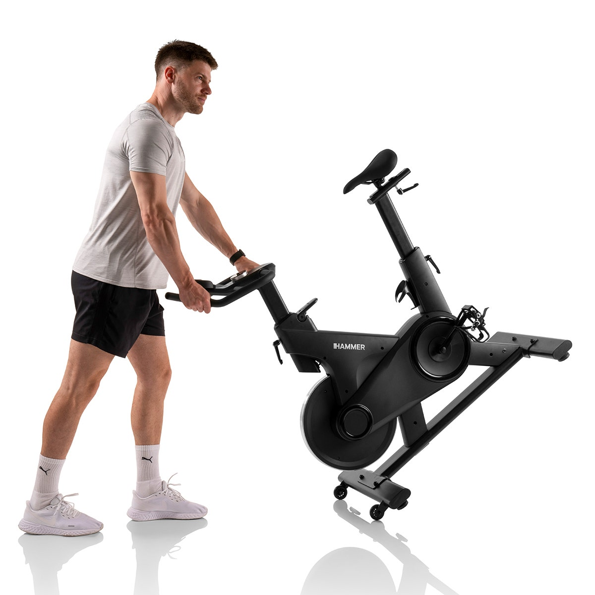 Un homme poussant un vélo d'exercice noir sur fond blanc.