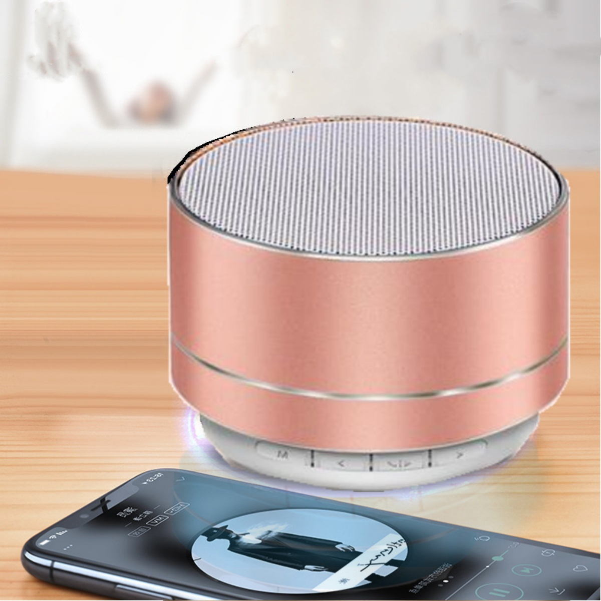 Ein roségoldener Lautsprecher auf einem Holztisch. Ein Smartphone zeigt eine Musik-Player-Oberfläche.