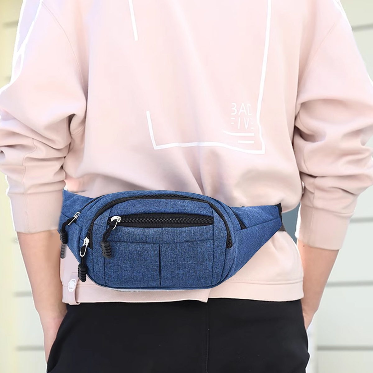 Eine blaue Bauchtasche, die von einer Person von hinten getragen wird. Die Person trägt einen rosa Pullover.