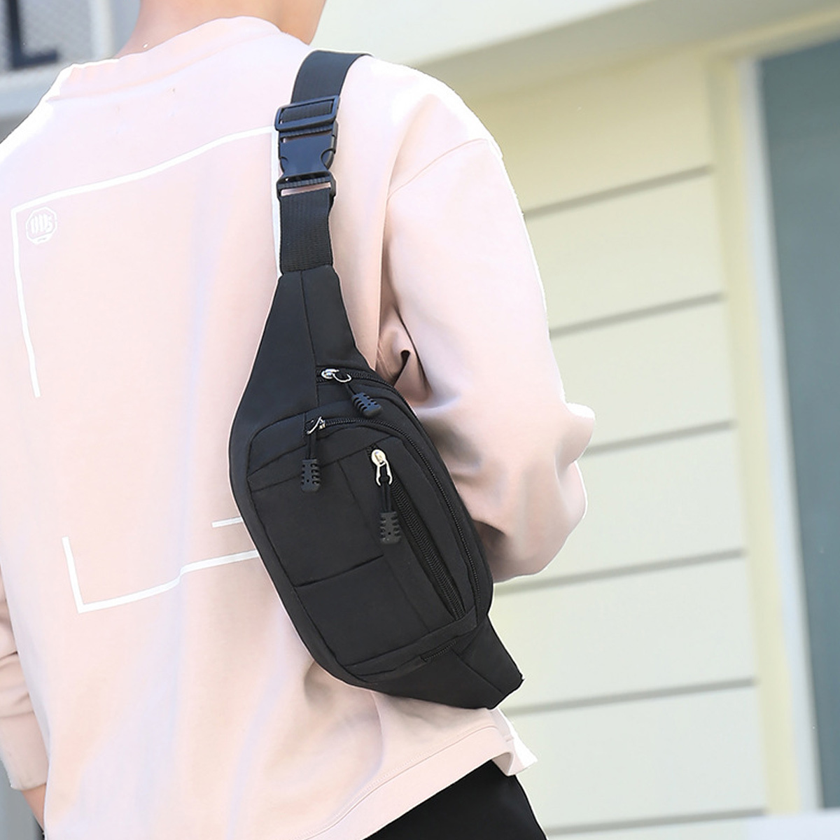Schwarze Bauchtasche von einer Person getragen, neutraler Hintergrund.