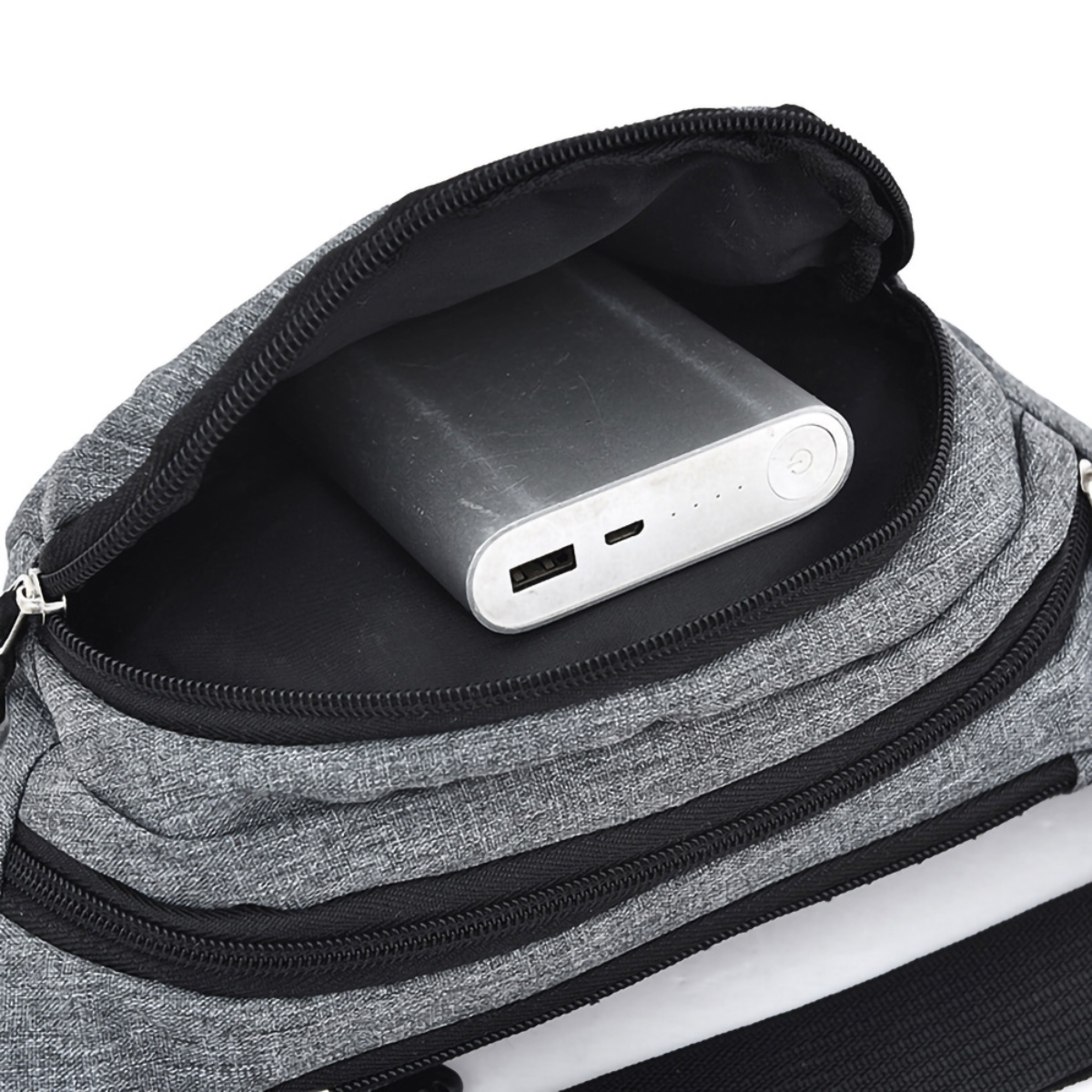 Eine graue Bauchtasche ist geöffnet und zeigt eine silberne Powerbank. Schwarzer Reißverschluss und Träger sind sichtbar.