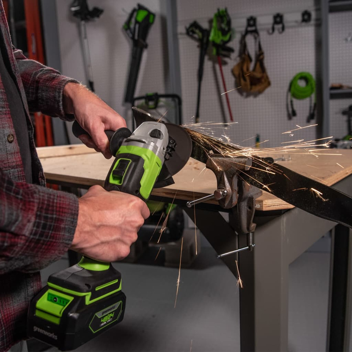 Mężczyzna używający zielono-czarnej szlifierki kątowej na metalowym pręcie, iskry lecą.