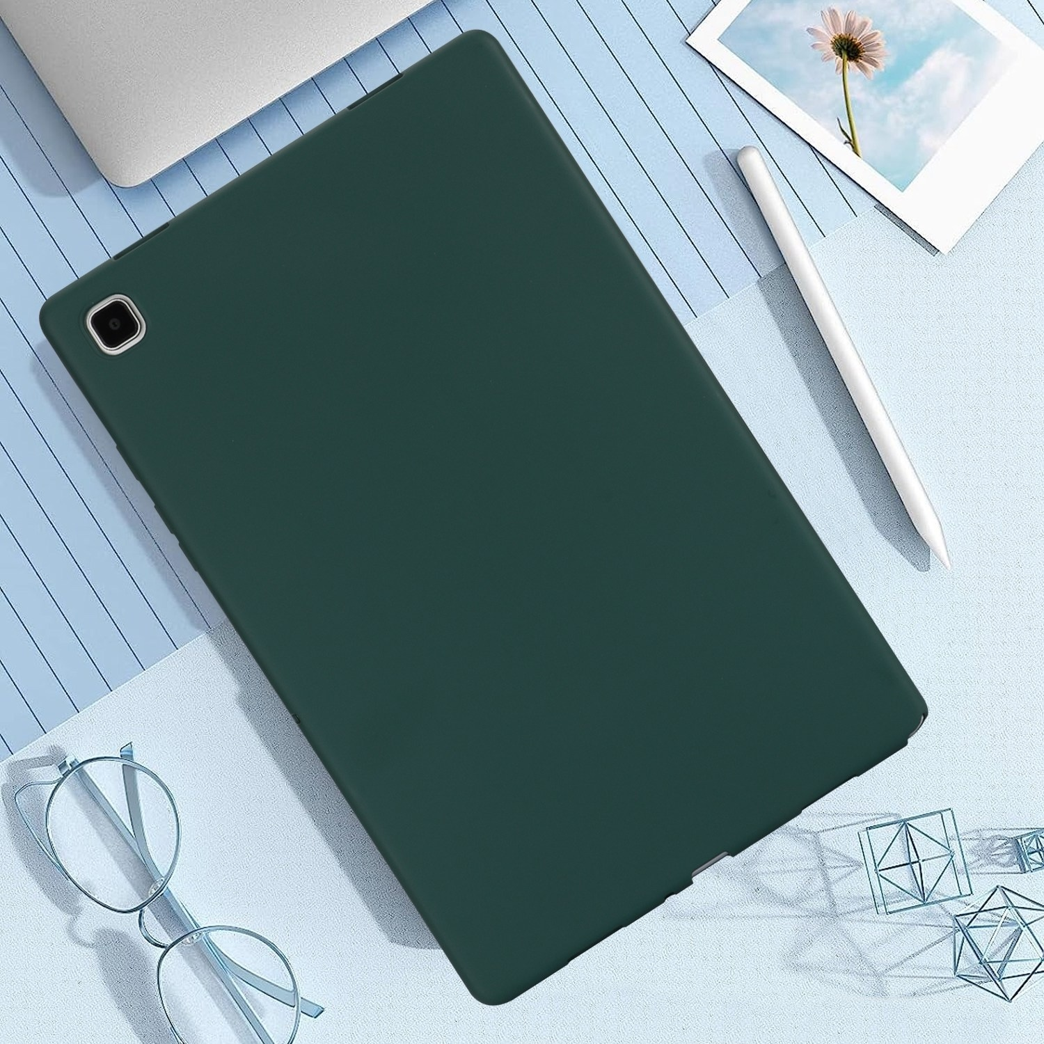 Ein grünes Tablet und ein weißer Stift liegen auf einer blauen Oberfläche mit Brille und geometrischen Formen.