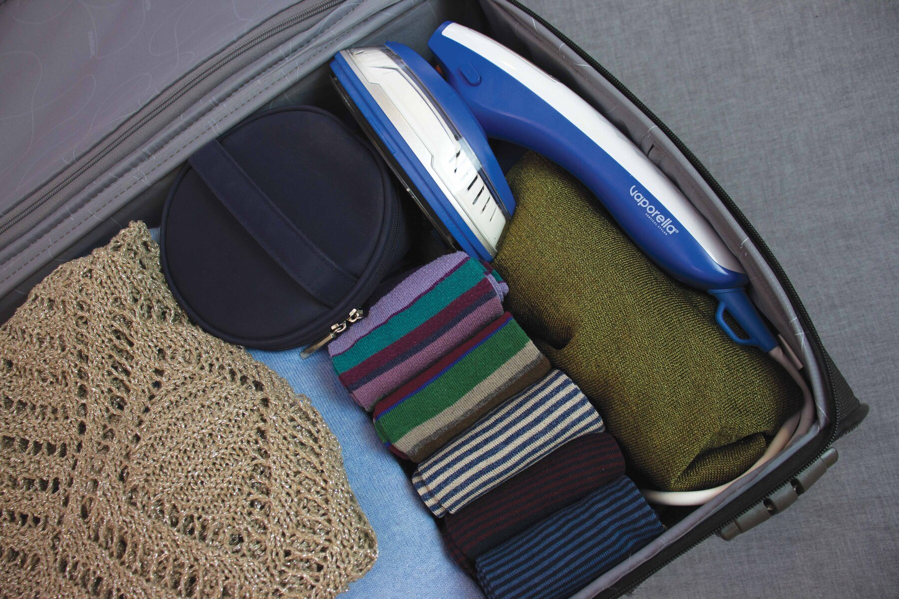 Una valigia aperta con vestiti, uno steamer e altri accessori da viaggio.