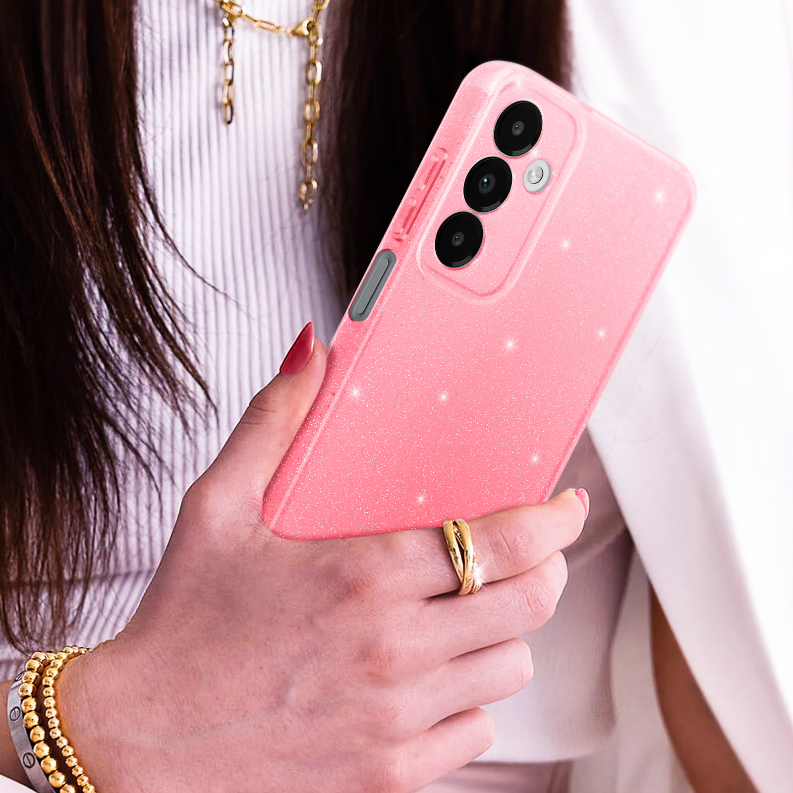 Custodia per telefono rosa glitterata con configurazione a tripla fotocamera, tenuta da una persona con un anello d'oro.