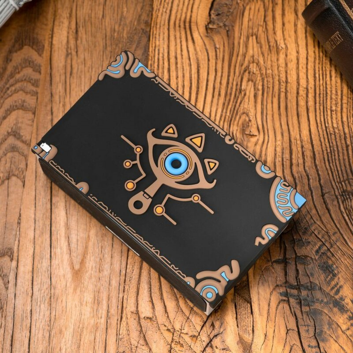 Schwarze Box mit stilisiertem Augendesign auf Holzoberfläche, mit Text.