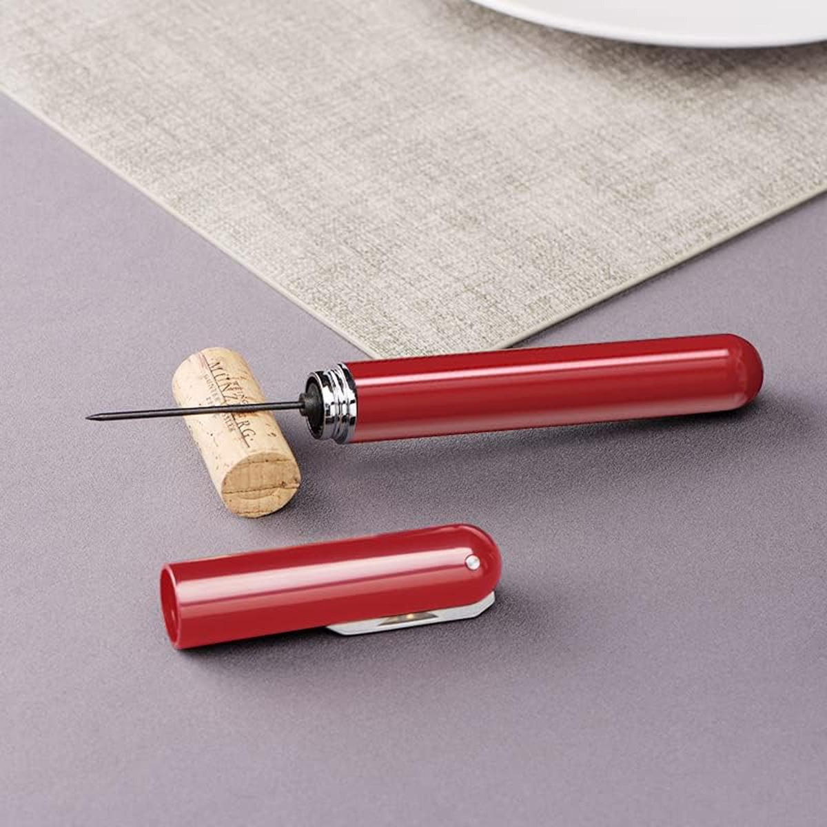 Roter Weinöffner und Korken. Der Öffner ist aus rotem Metall und hat einen Korkenzieher.