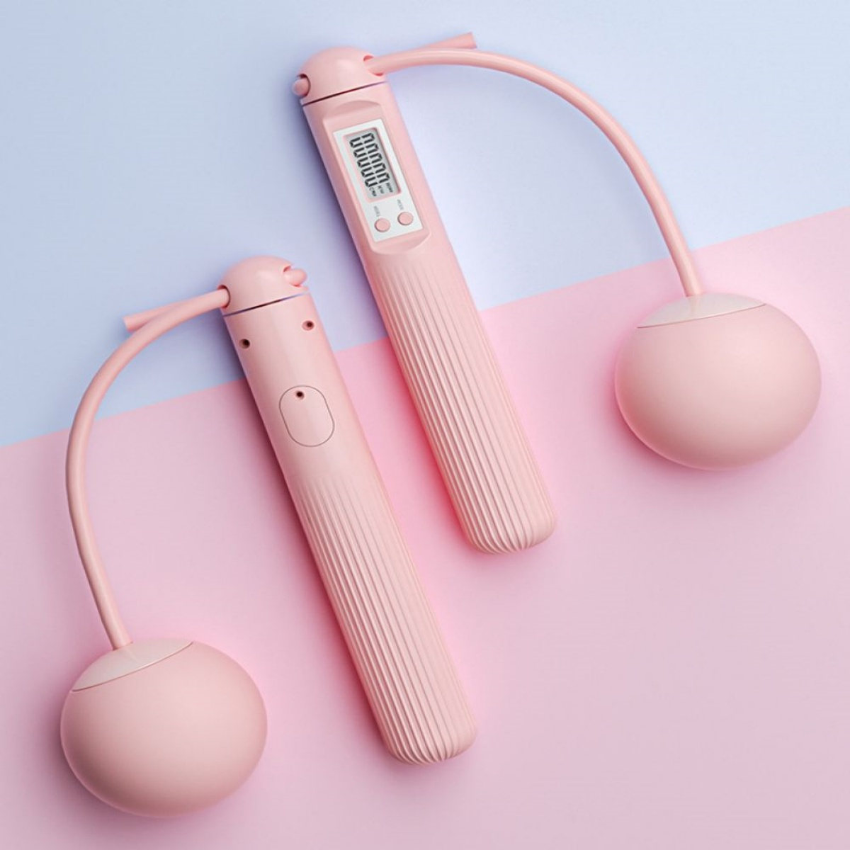 Zwei rosa Springseile mit Digitalanzeigen, liegen auf einer rosa und blauen Oberfläche.