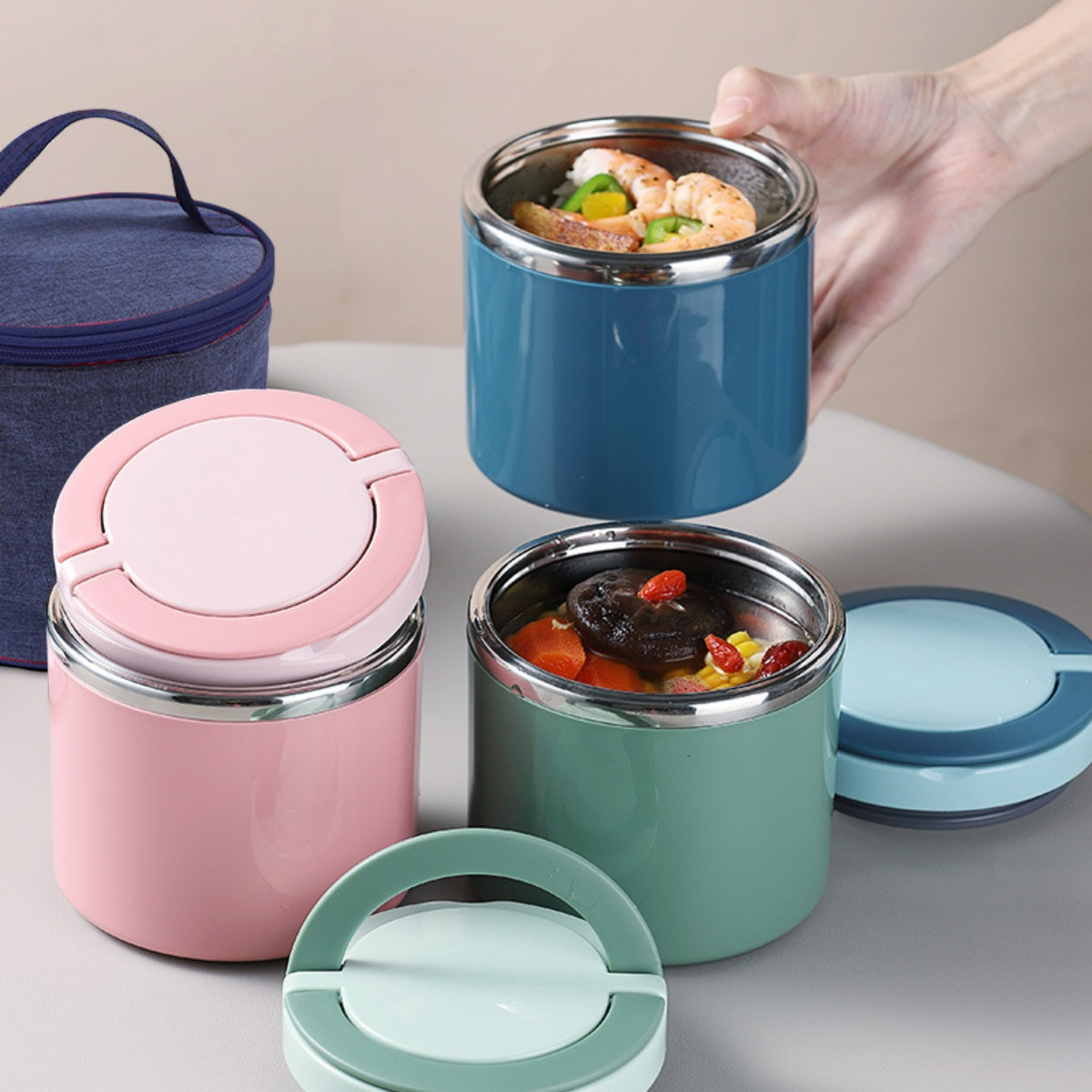 Drei Lunchboxen mit Essen, eine rosa, eine teal, eine blau, mit einer Tasche.