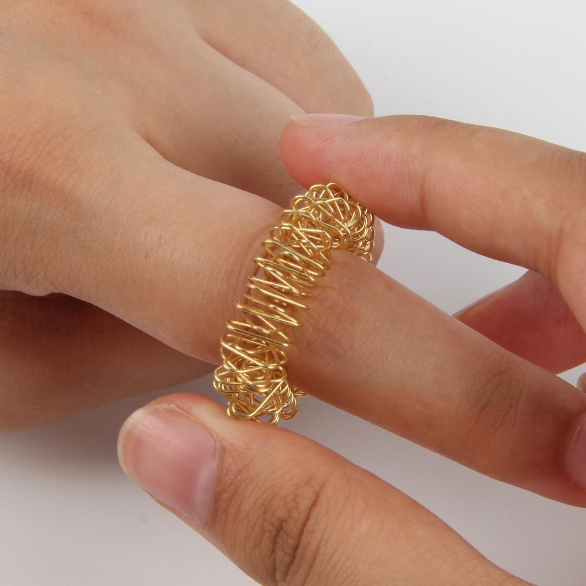 Ein Finger einer Person mit einem goldenen Fingermassagegerät. Das Massagegerät ist ein Ring aus Draht.