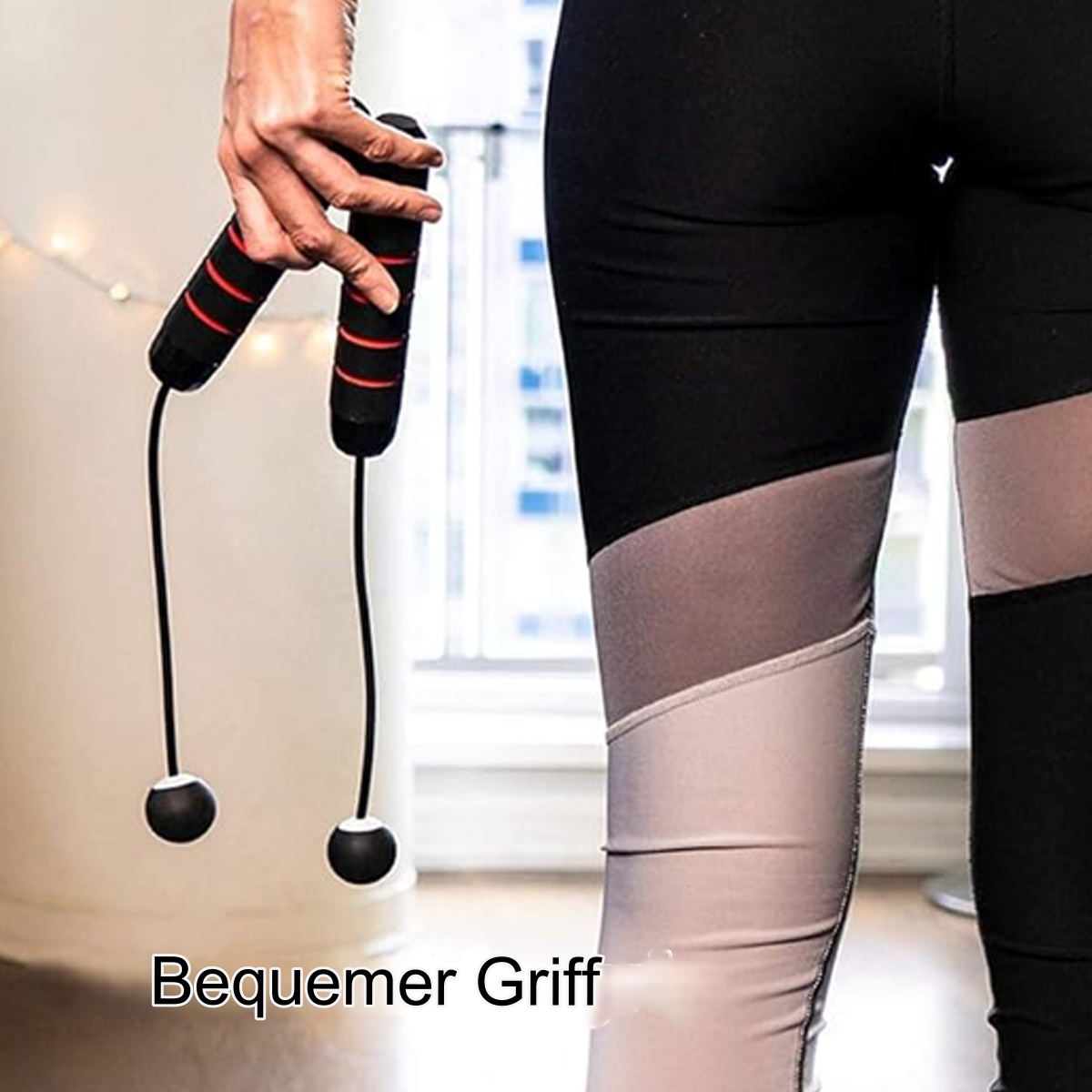 Eine Person hält ein schwarzes Springseil mit roten Griffen, trägt schwarze Leggings mit grauen Einsätzen.