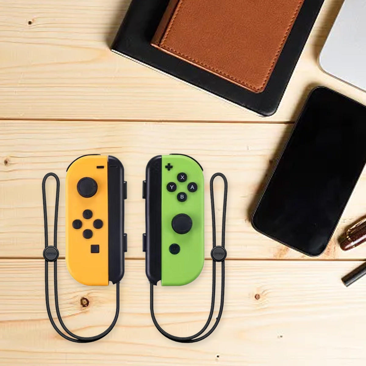 Zwei Gamecontroller, gelb und grün, auf einer Holzoberfläche. Ein Notizbuch und Telefon liegen daneben.