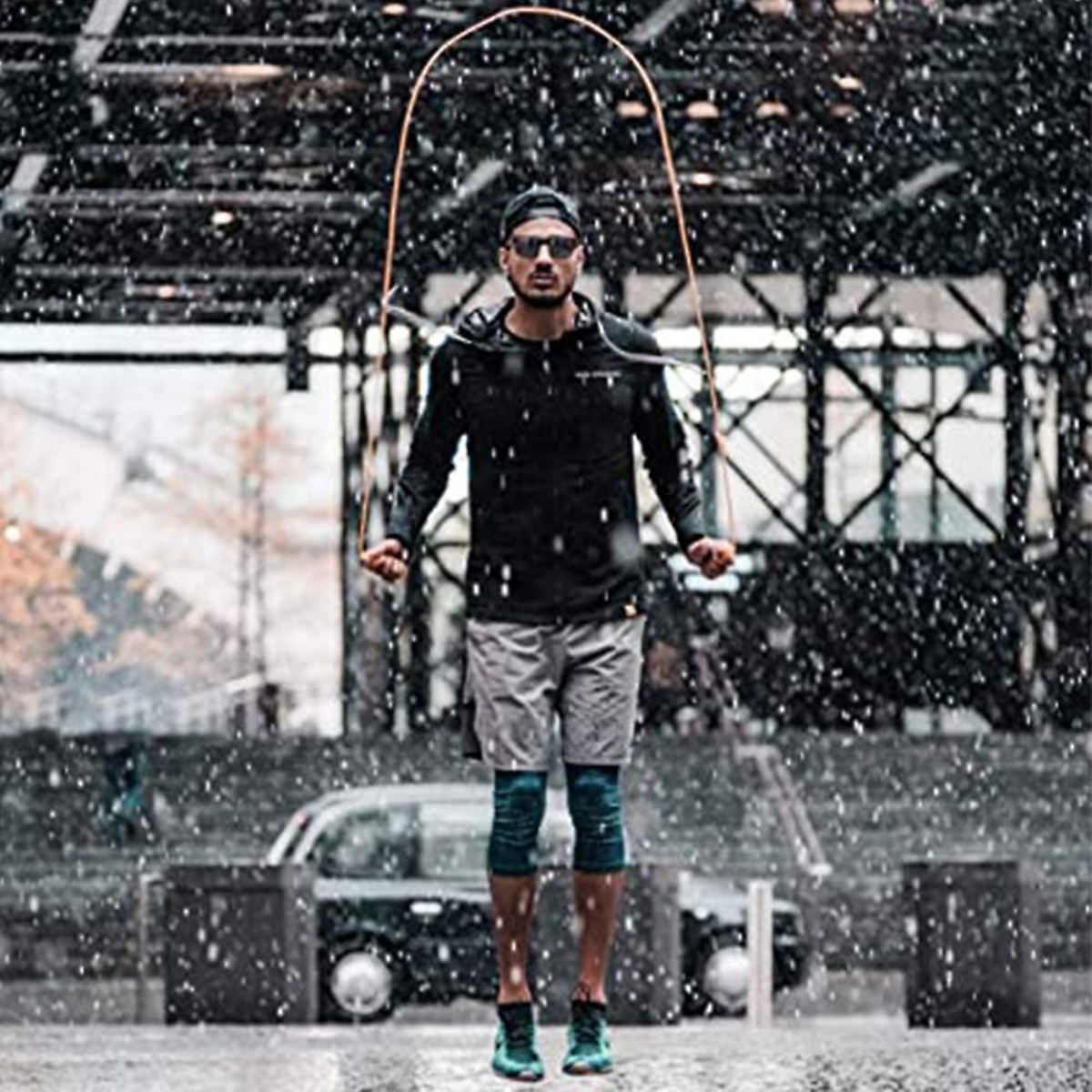 Ein Mann springt im Regen Seil, trägt eine schwarze Jacke und Shorts. Der Hintergrund ist unscharf.