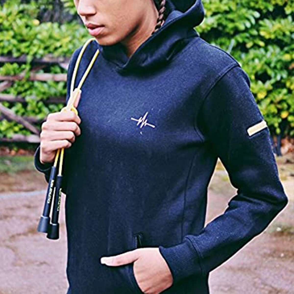Eine junge Person in einem marineblauen Kapuzenpullover hält draußen ein gelbes Springseil.