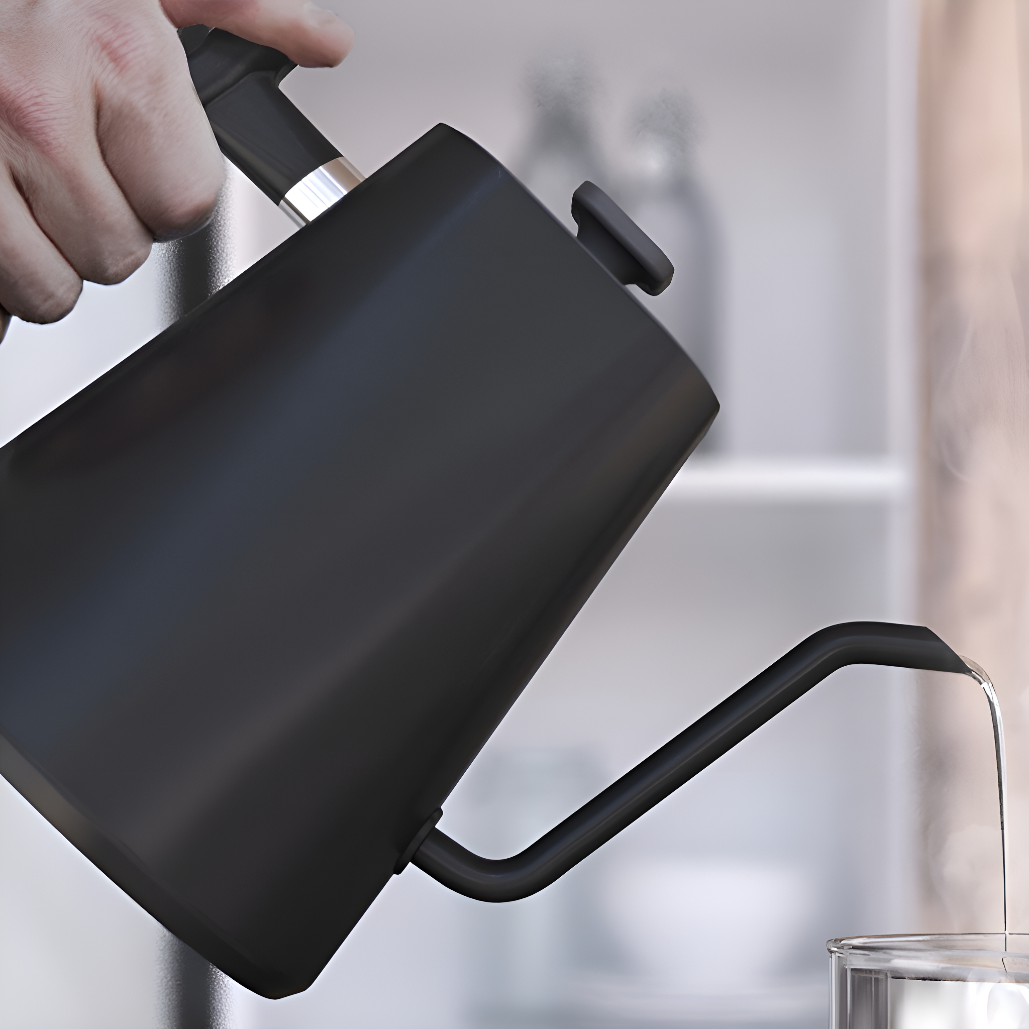 Schwarzer Wasserkocher gießt Wasser in ein Glas, unscharfer Hintergrund.