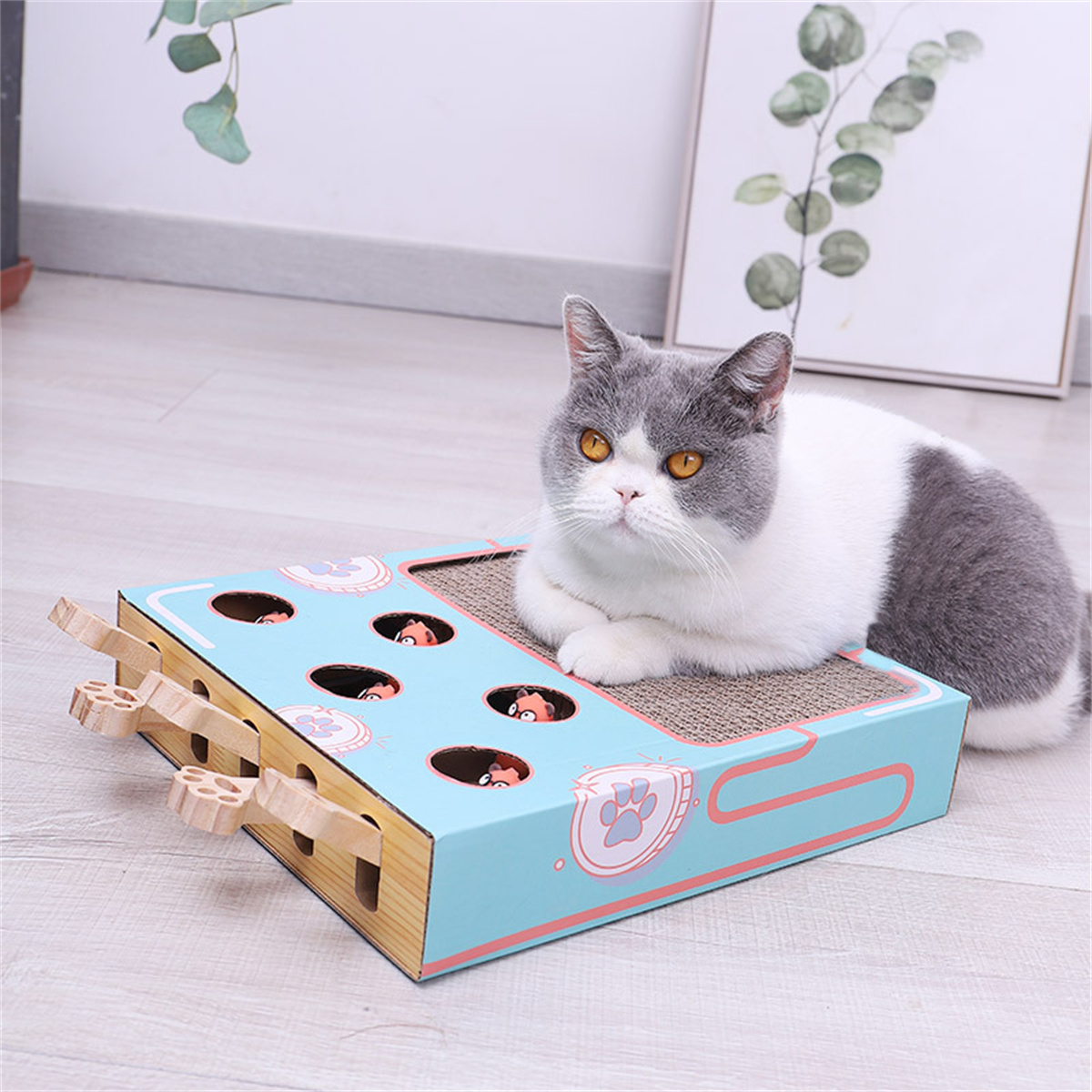 Katze sitzt auf einem Katzenspielzeug mit Löchern, aus denen Spielfiguren herausschauen.