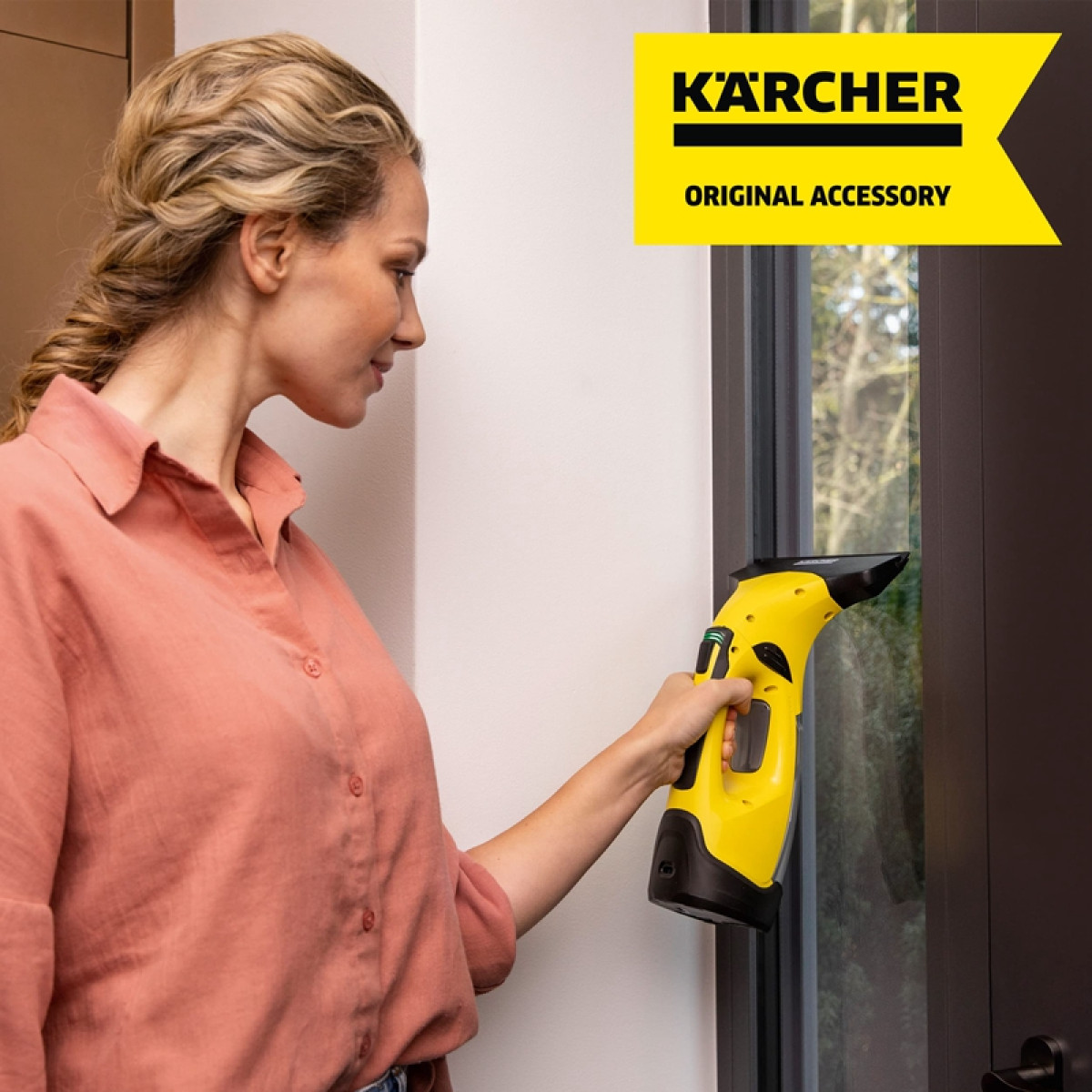 Kobieta czyści okno żółtą myjką do okien Karcher. Obecne logo i tekst Karcher.