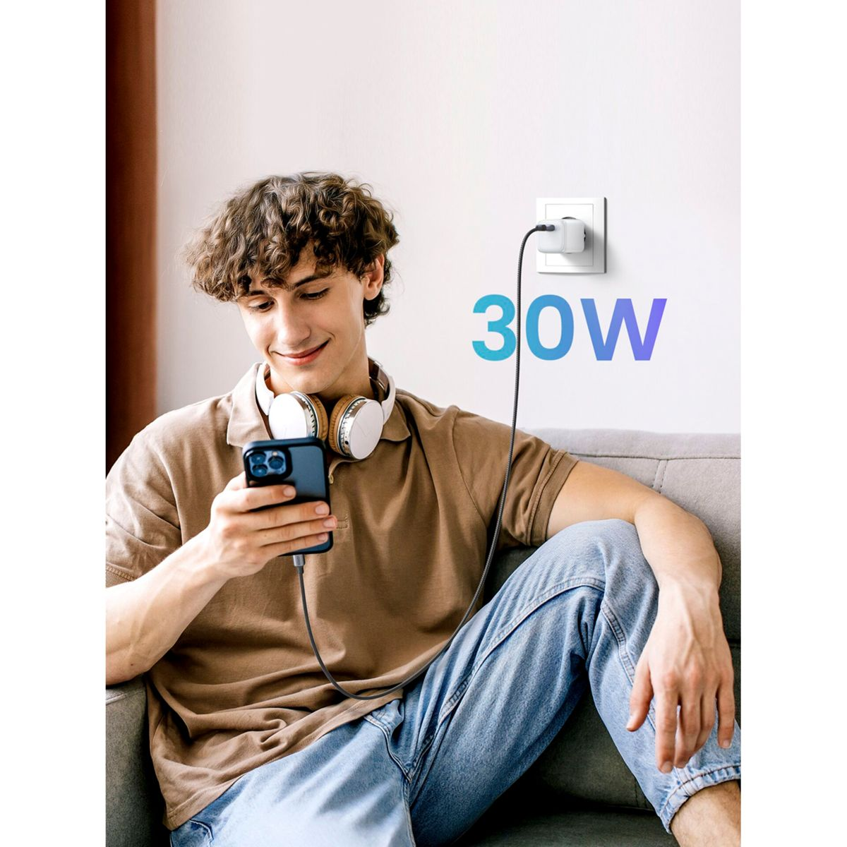 Mężczyzna używa telefonu podczas ładowania go ładowarką 30W, która jest podłączona do ściany.