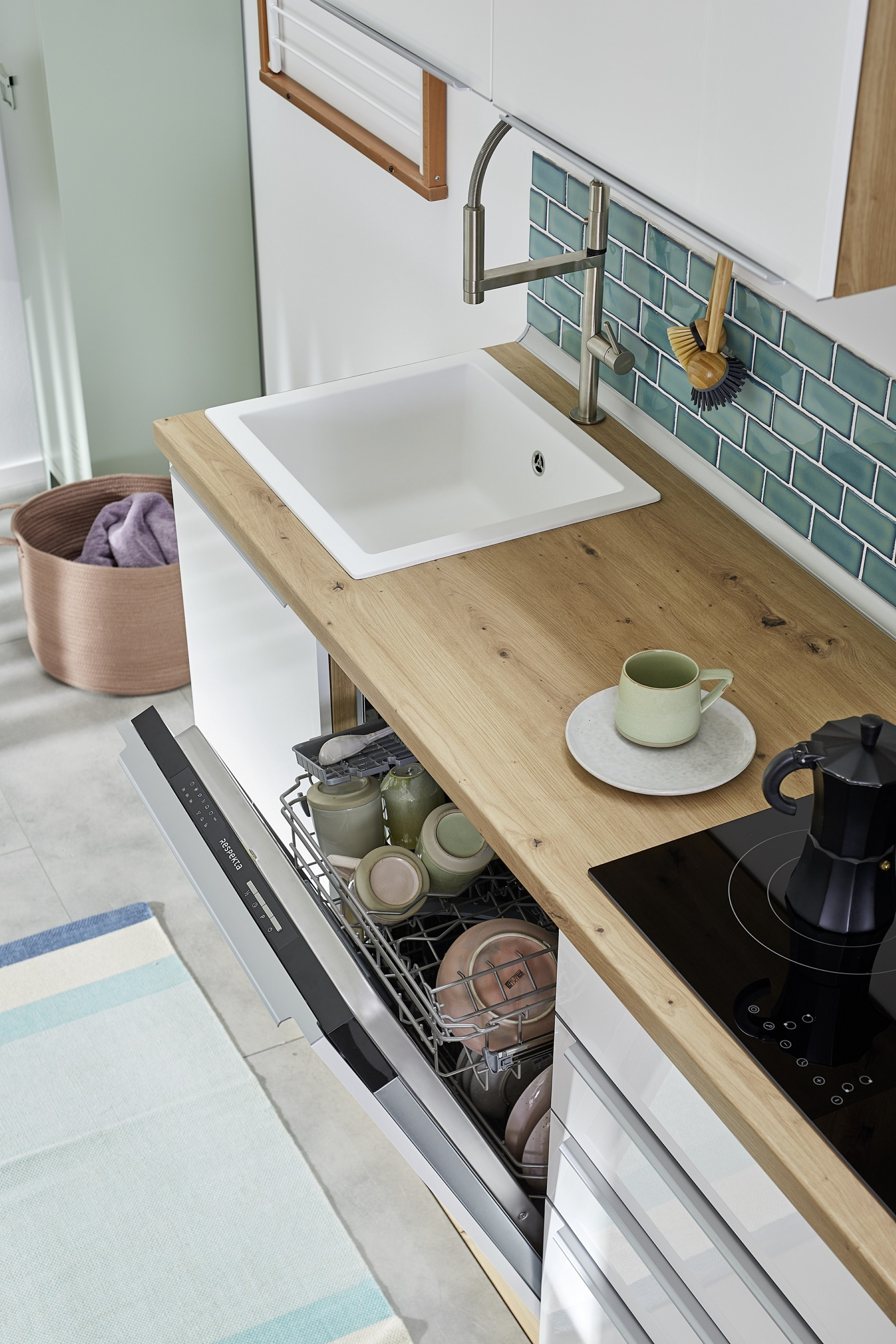 Kücheninnenraum mit Spüle, Geschirrspüler und Arbeitsplatte mit Tasse und Kaffeemaschine. Blaue Fliesen.