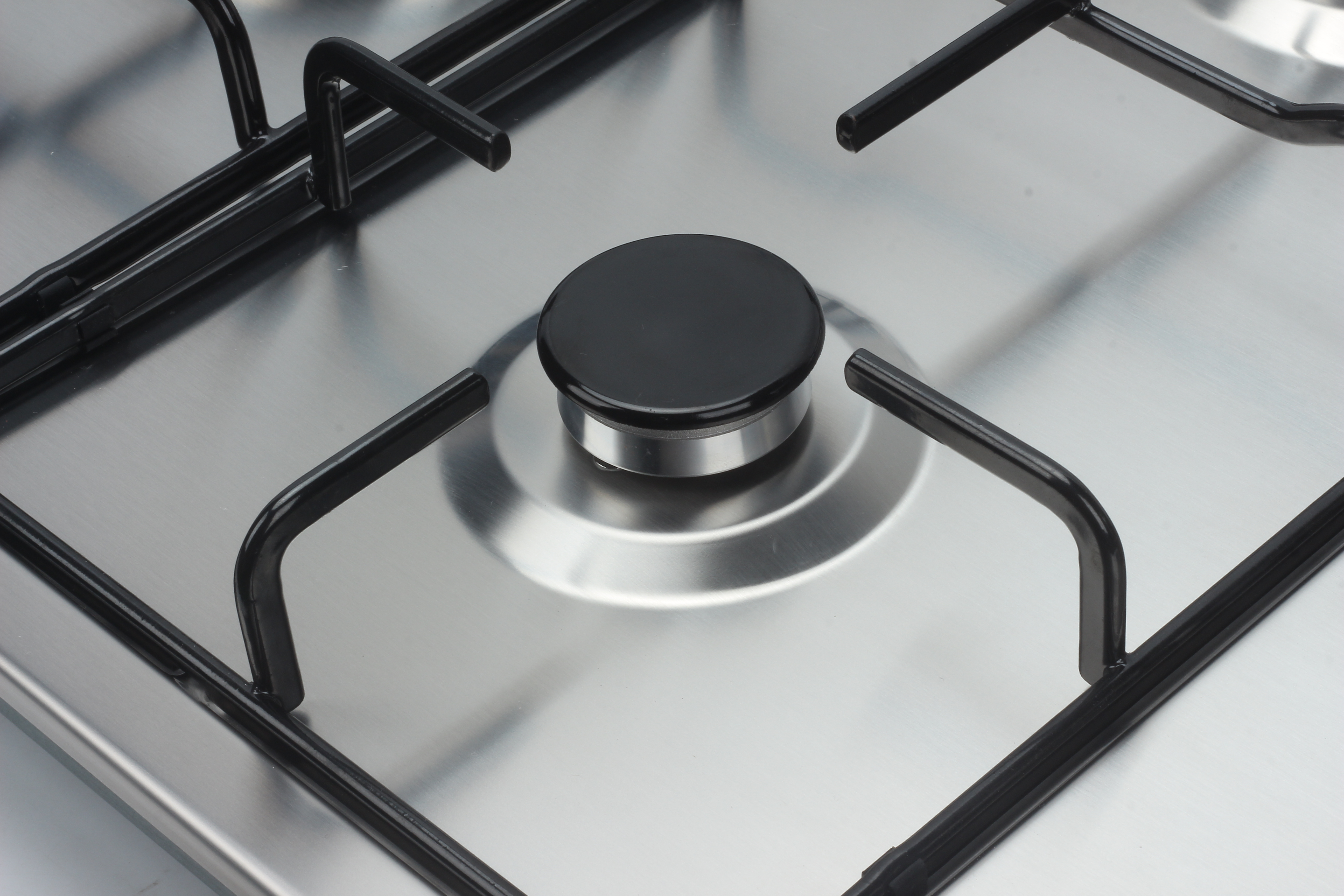 Primer plano de una placa de gas de acero inoxidable con rejilla de metal negro y un mando negro.