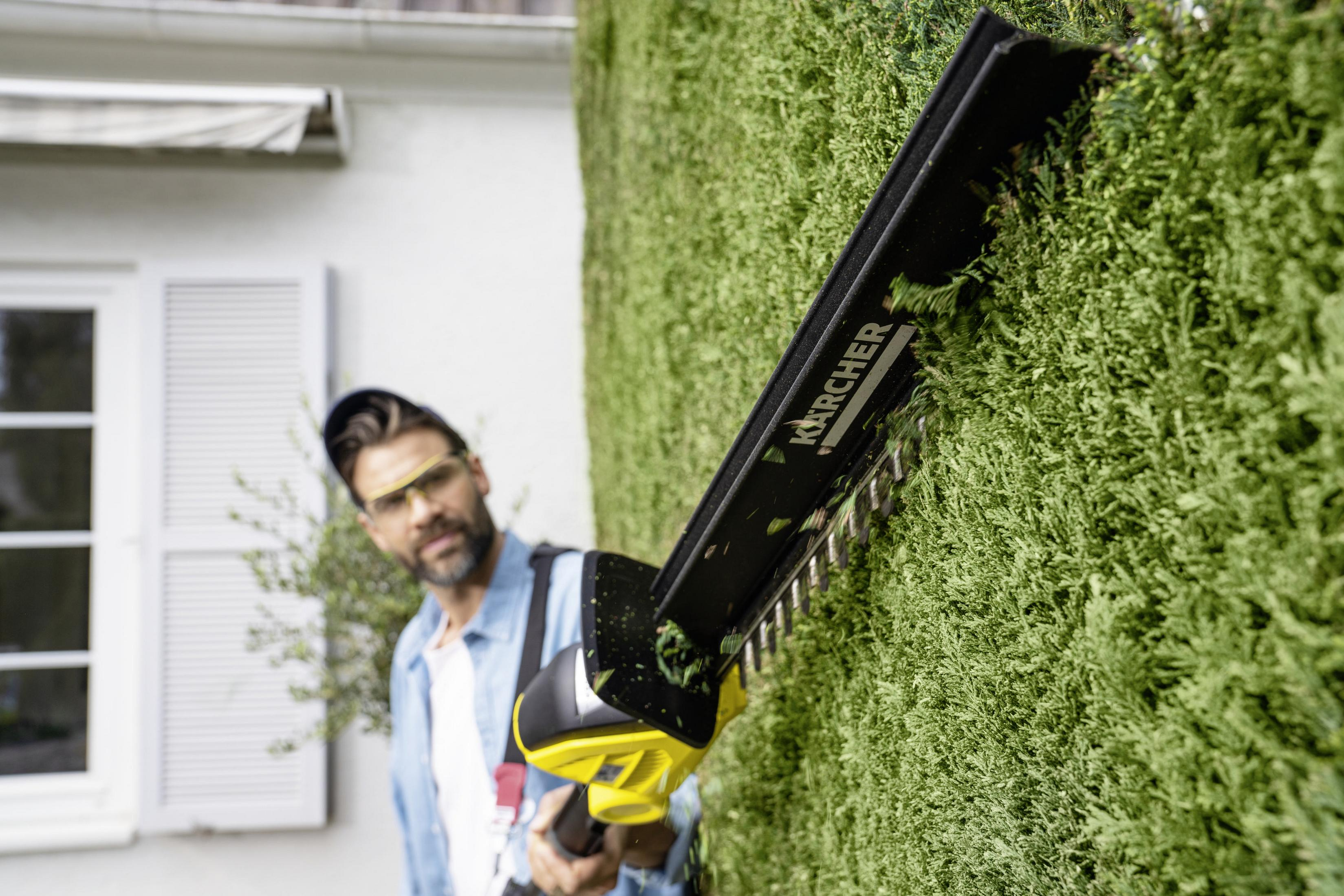 Un hombre podando un seto con un cortasetos eléctrico. El dispositivo tiene un diseño negro y amarillo.
