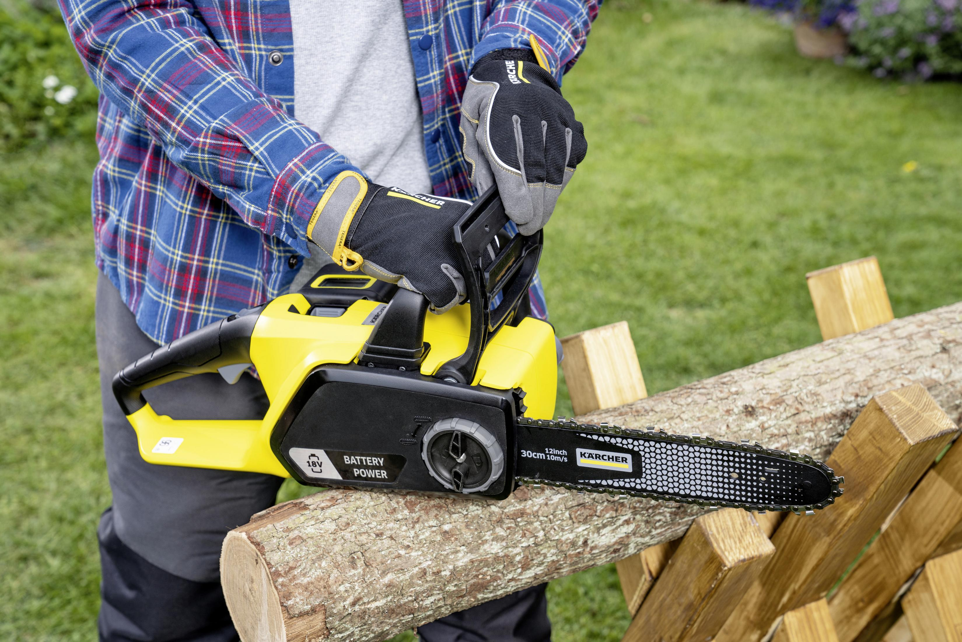 Osoba w rękawicach używa żółtej piły łańcuchowej do cięcia kłody na drewnianym kozle.