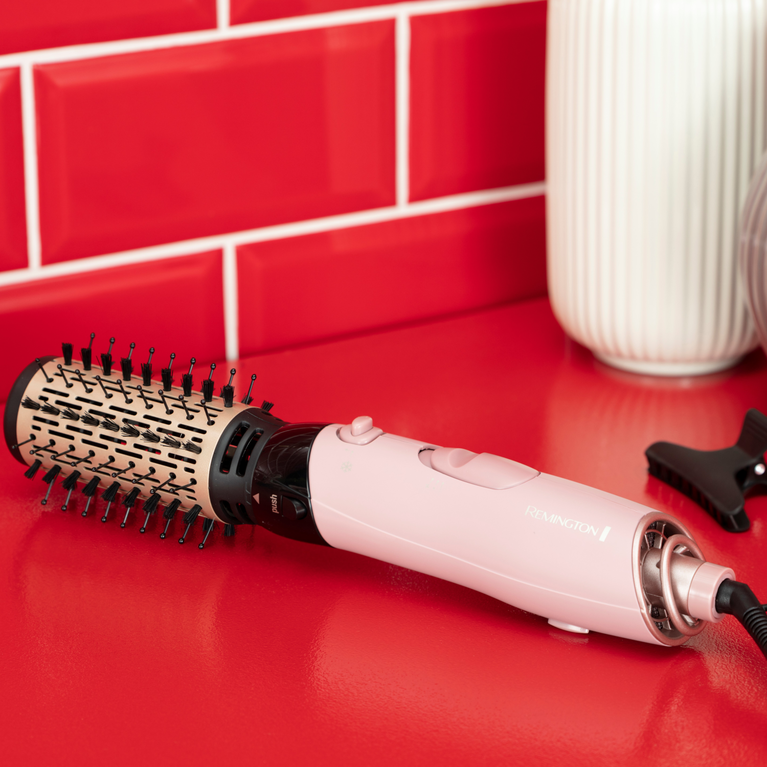 Spazzola per capelli rosa su una superficie rossa. Parete rossa e vaso sullo sfondo.