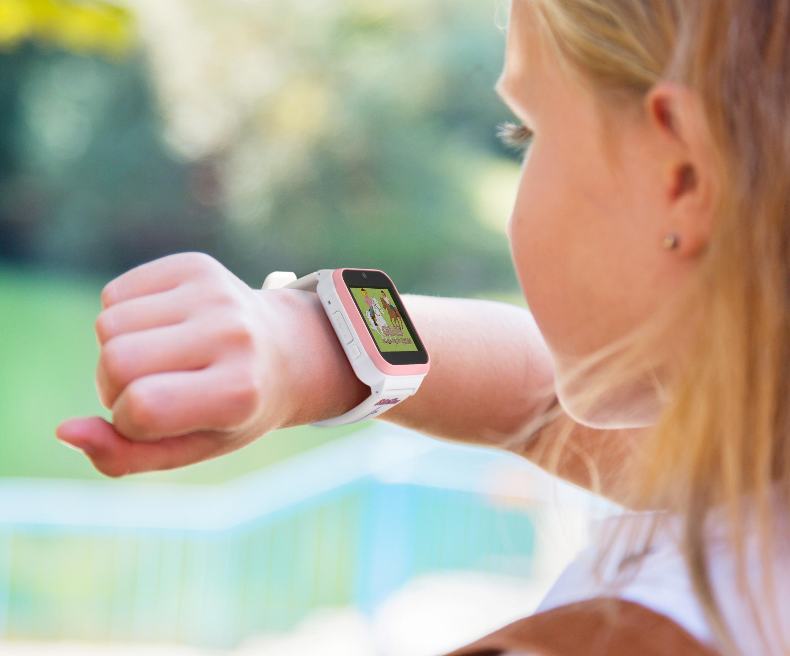 Ein Mädchen betrachtet eine rosa-weiße Smartwatch an ihrem Handgelenk. Der Bildschirm ist an.