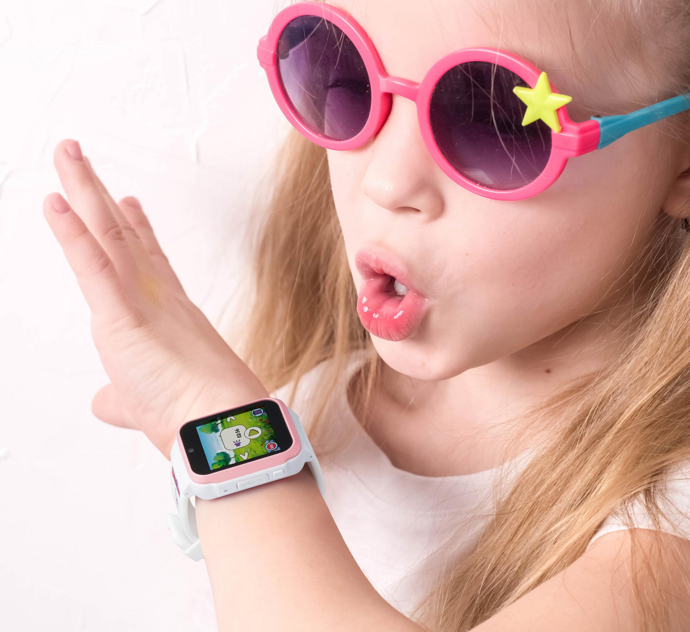 Junges Mädchen mit rosafarbener Sonnenbrille und Smartwatch. Sie schaut auf die Uhr und hat einen aufgeregten Ausdruck.