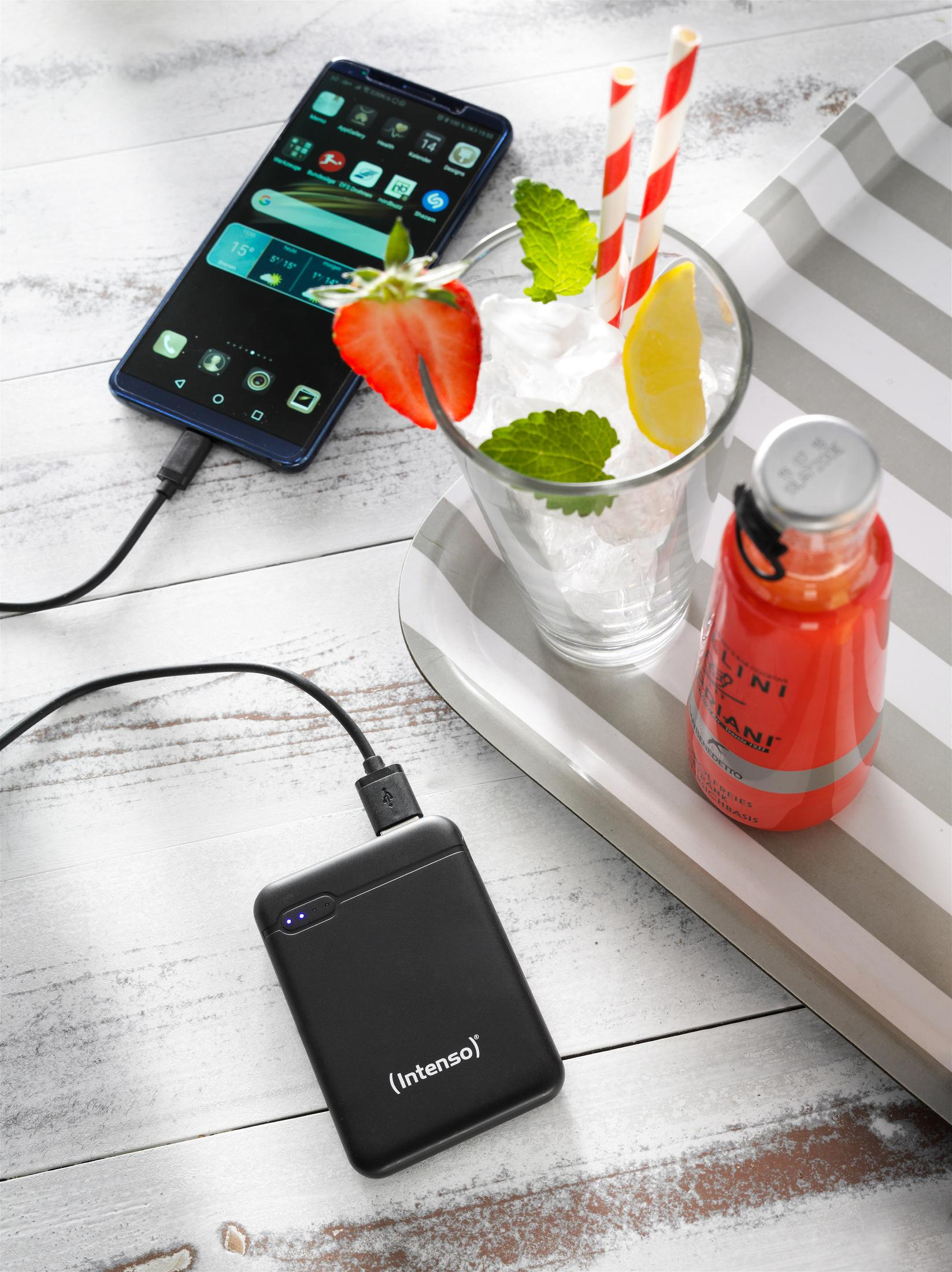 Een tafel met een telefoon die oplaadt, een drankje met ijs en een fles sap.