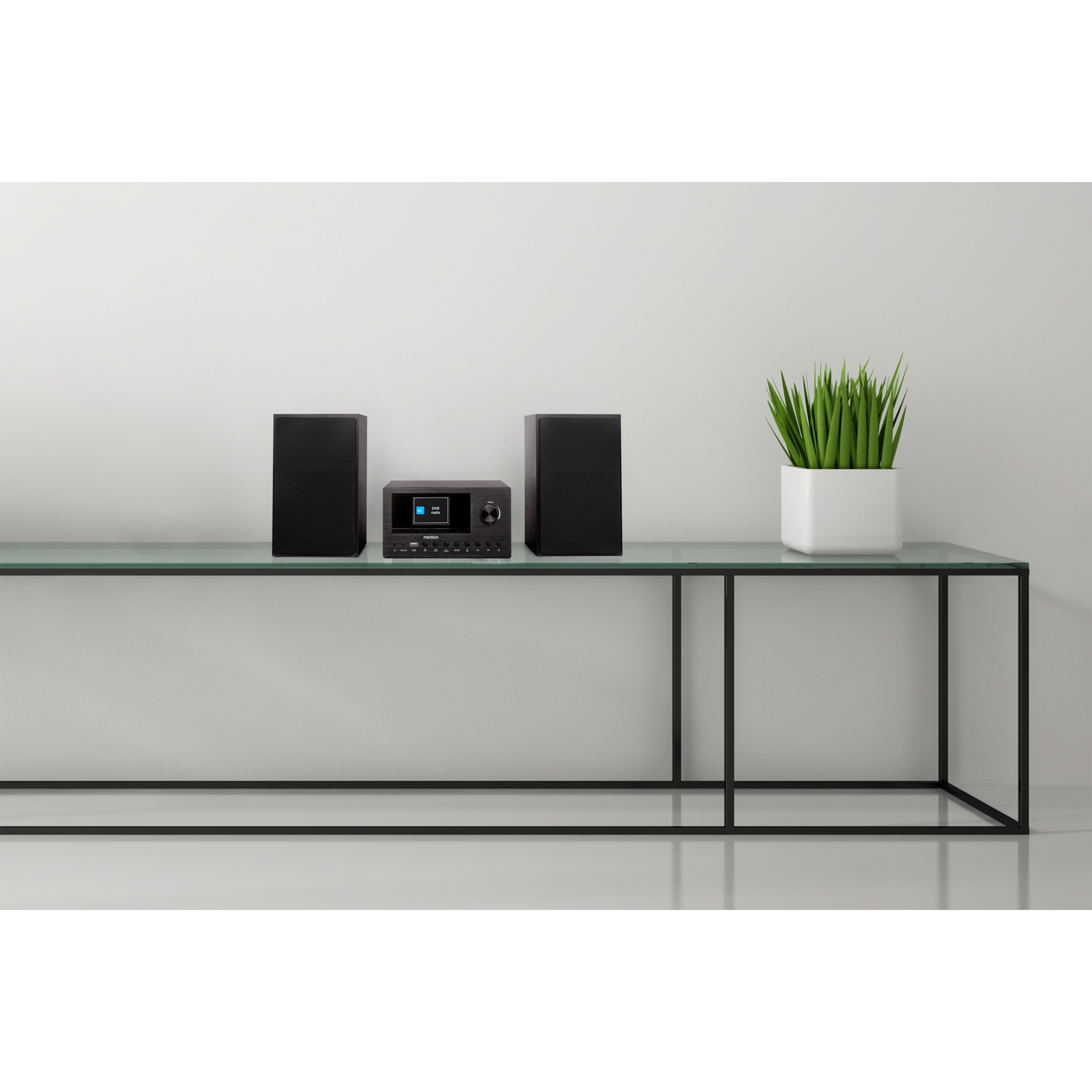 Un sistema de audio negro sobre una mesa de cristal, con dos altavoces negros y una planta.