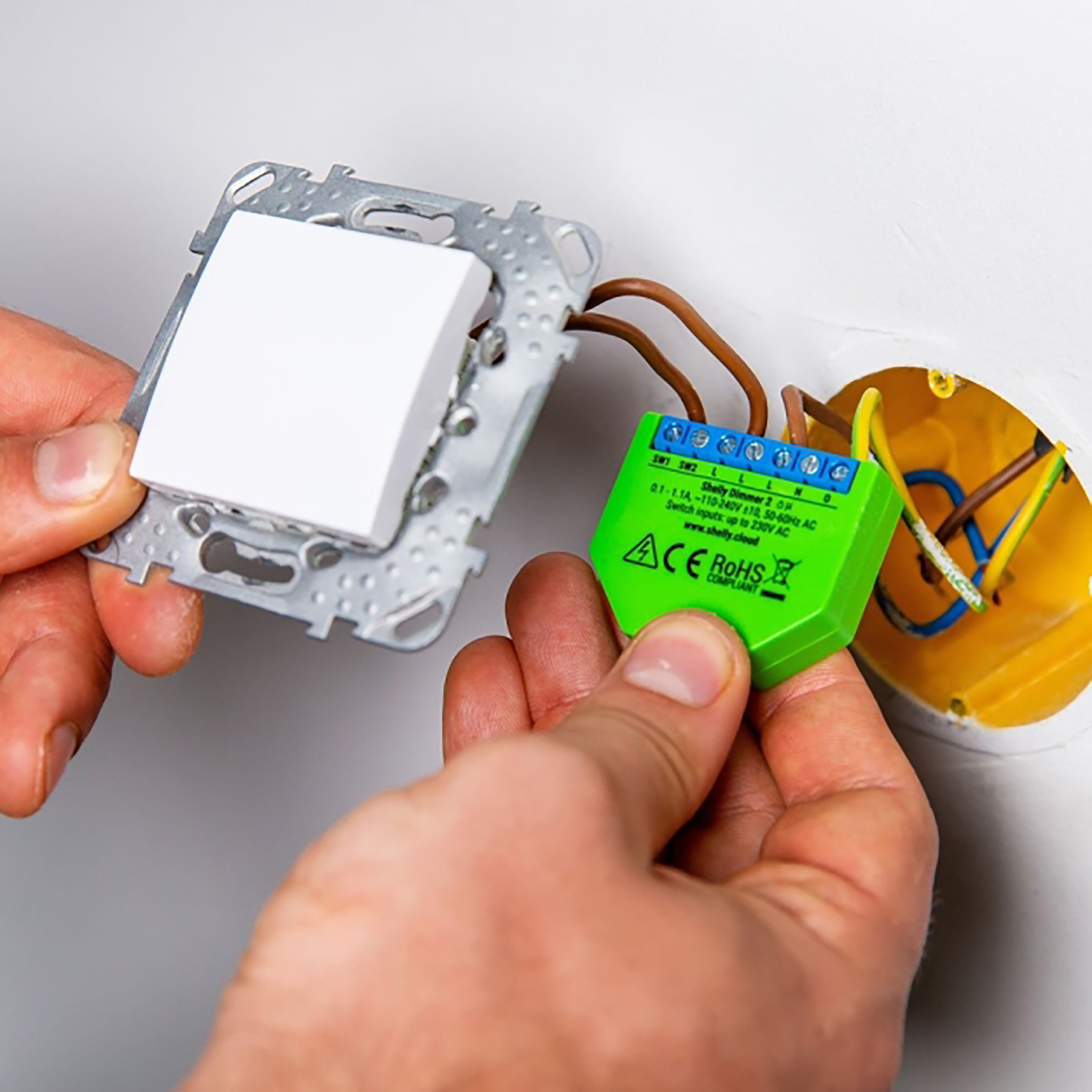 Una persona instalando un interruptor inteligente verde en un enchufe de pared.