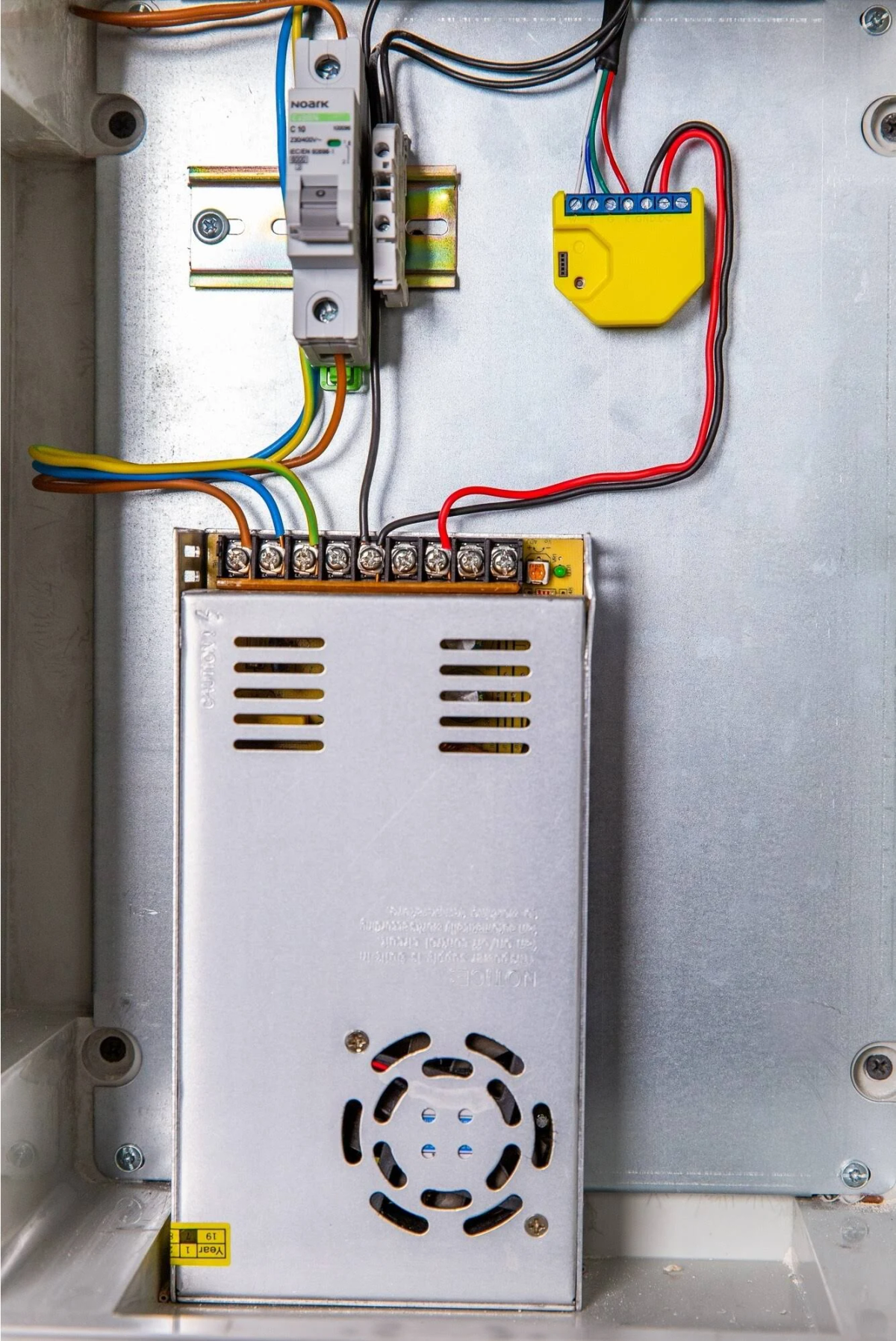 Caja metálica abierta con componentes eléctricos, cables y fuente de alimentación. Un relé amarillo es visible.