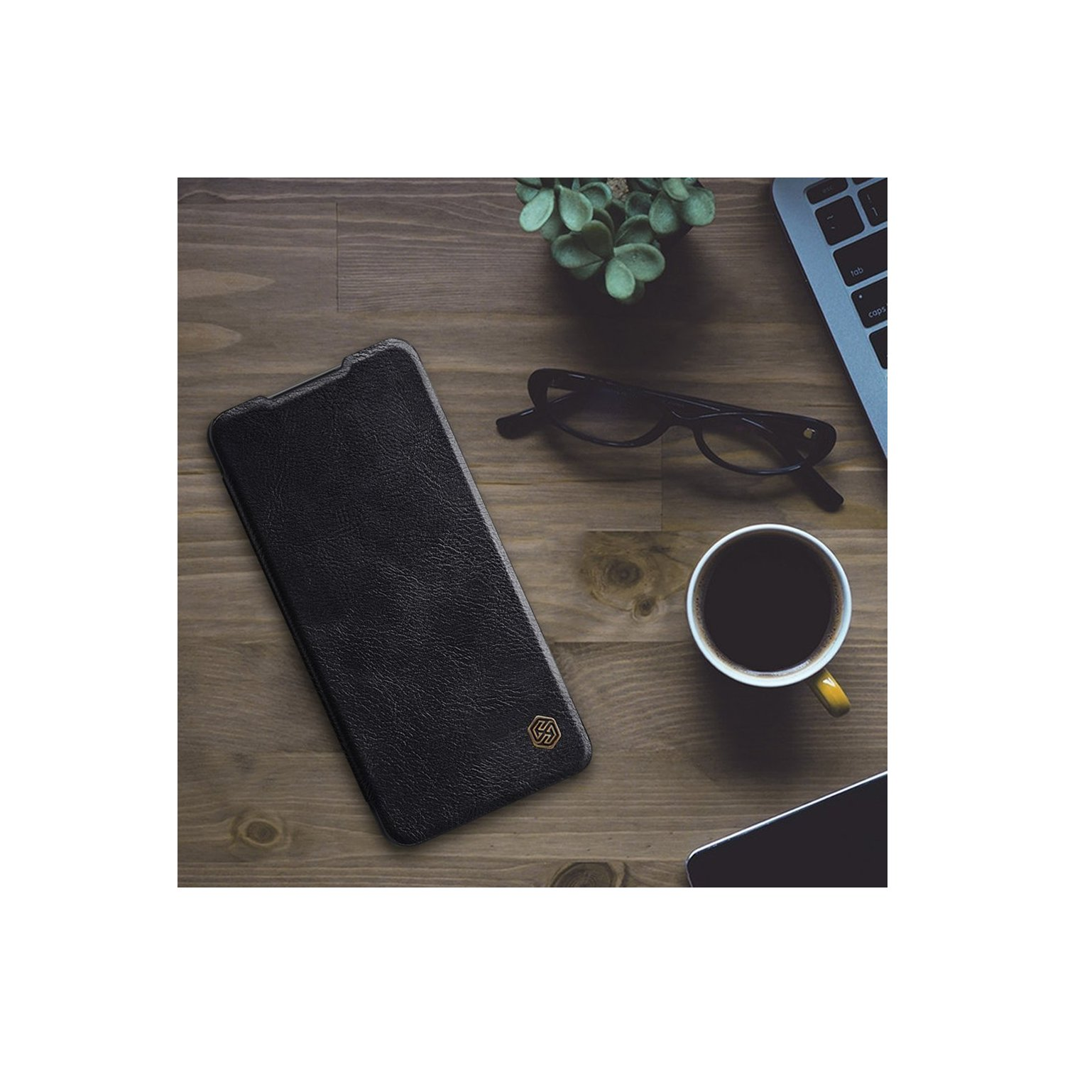 Schwarze Handyhülle auf einem Holztisch. Ein Notizbuch, eine Brille und eine Tasse Kaffee sind ebenfalls vorhanden.