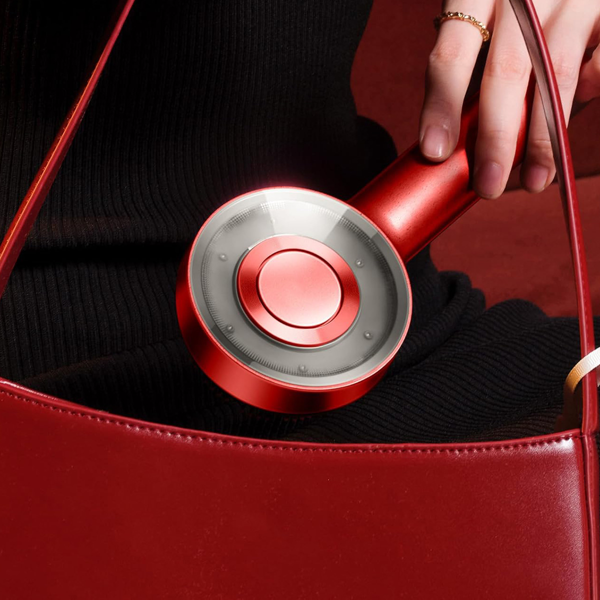 Una herramienta roja para el cabello es sostenida por una mano. Un bolso rojo en el fondo.