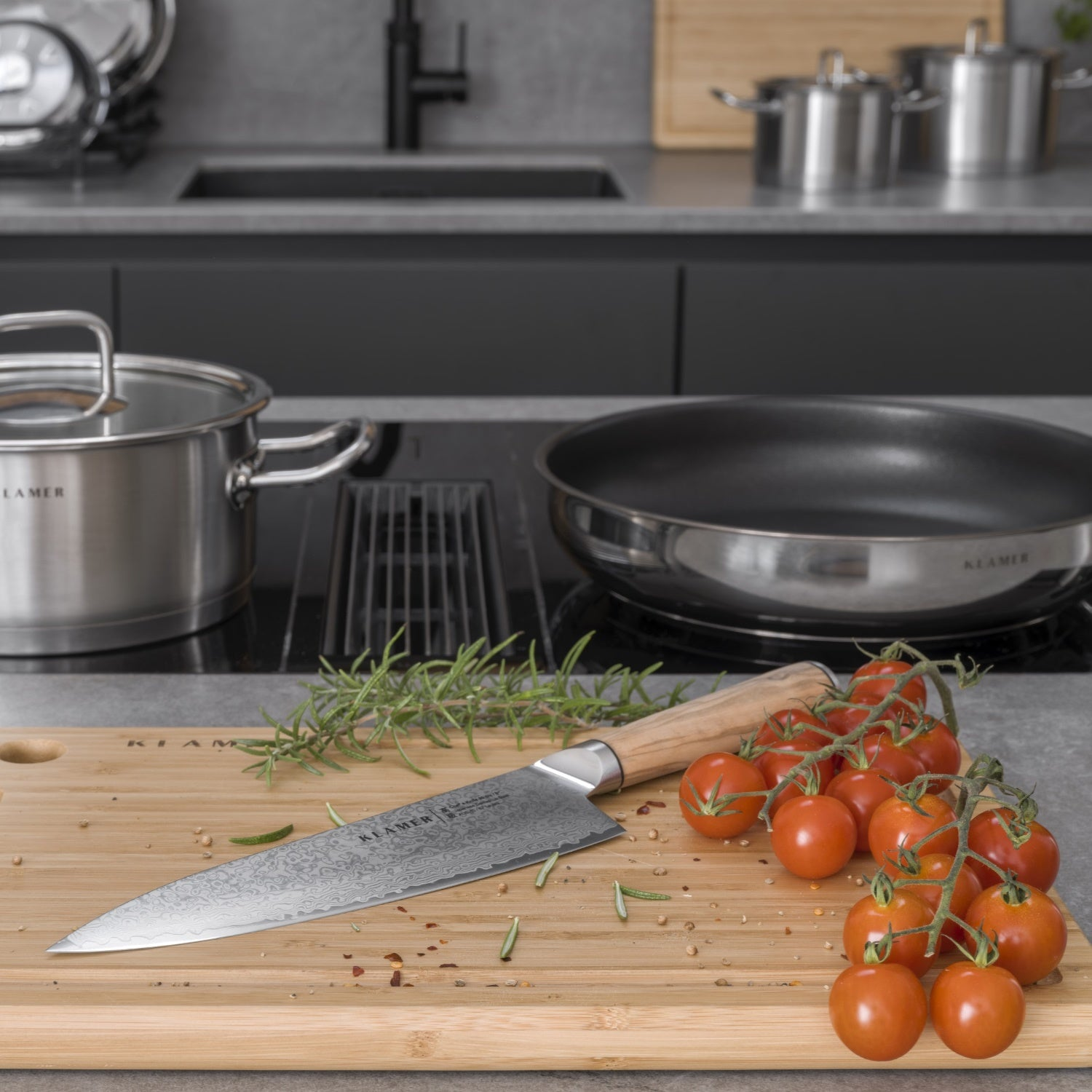 Messer auf einem Schneidebrett mit Tomaten und Kräutern. Töpfe und eine Pfanne im Hintergrund.