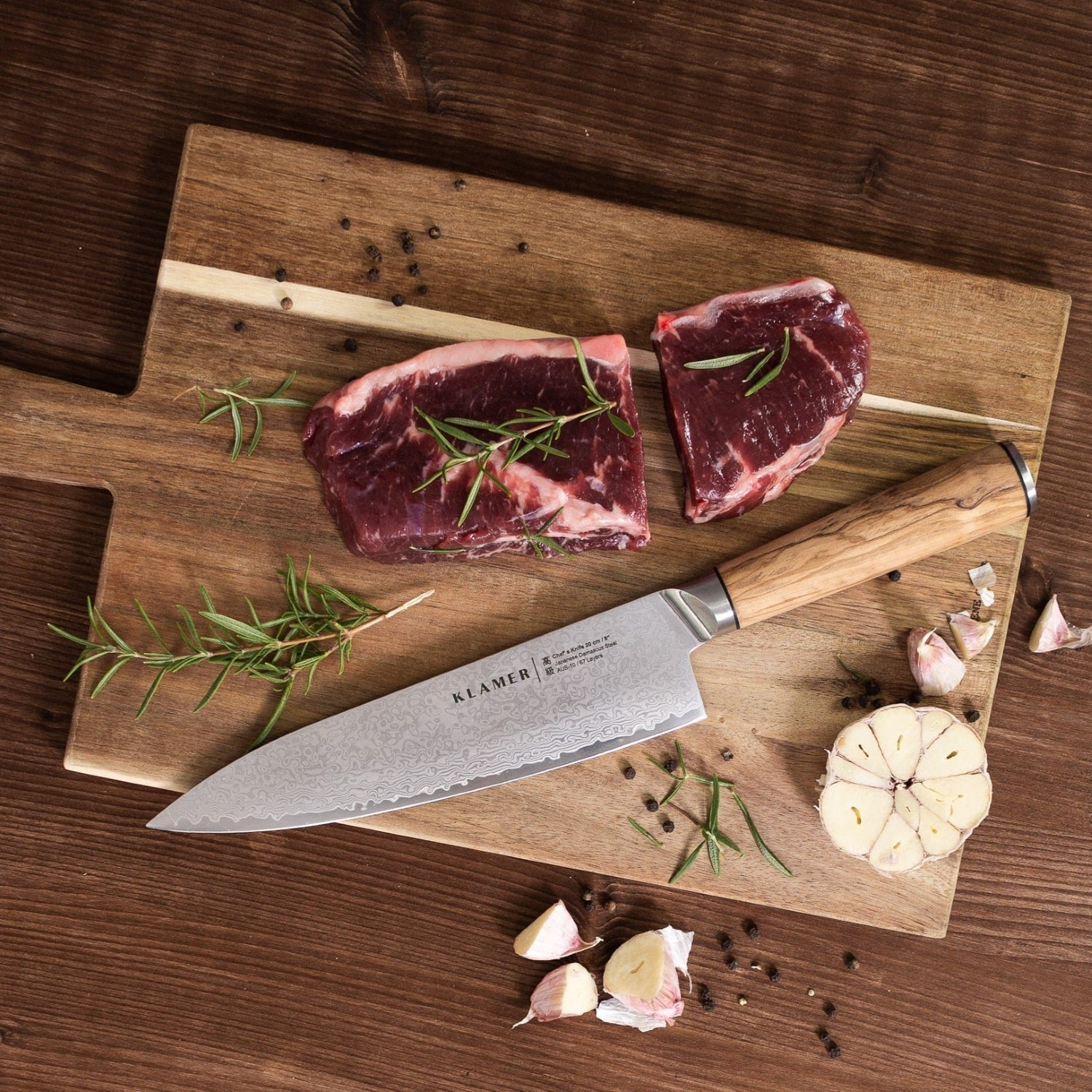 Rohe Steaks auf einem Holzbrett mit Messer, Rosmarin und Knoblauchzehen. Holz-Hintergrund.