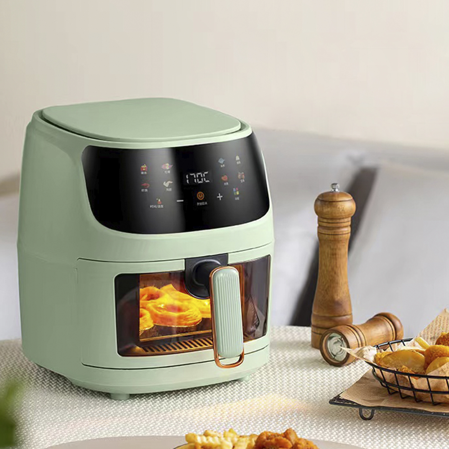 Ein mintgrüner Luftfritteuse mit Digitalanzeige, Essen drin und einem hölzernen Pfeffermühle in der Nähe.