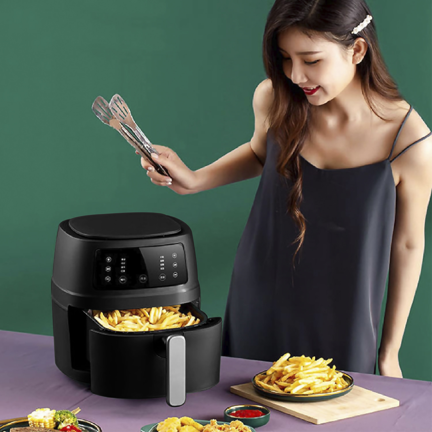 Donna che tiene le pinze su una friggitrice ad aria nera con patatine fritte cotte, altro cibo presente.