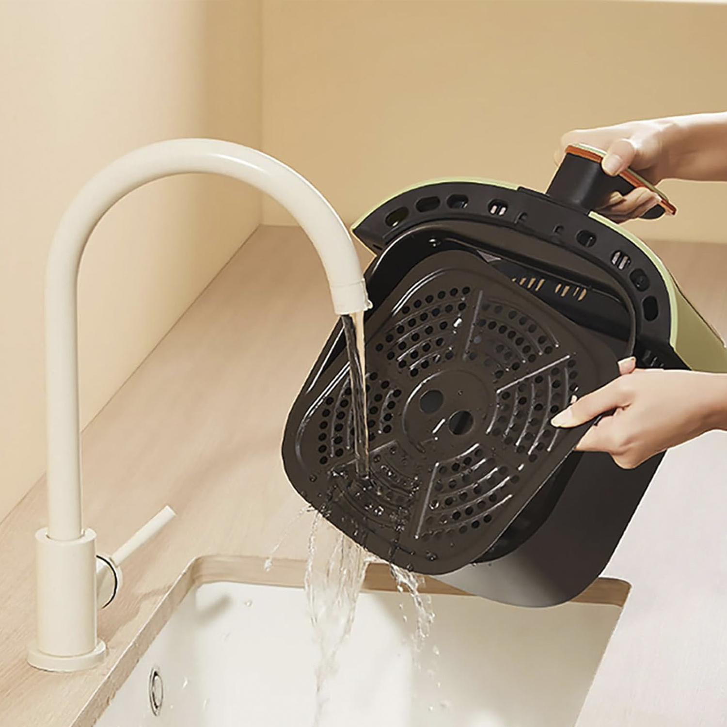Person wäscht den Frittierkorb unter einem Wasserhahn.