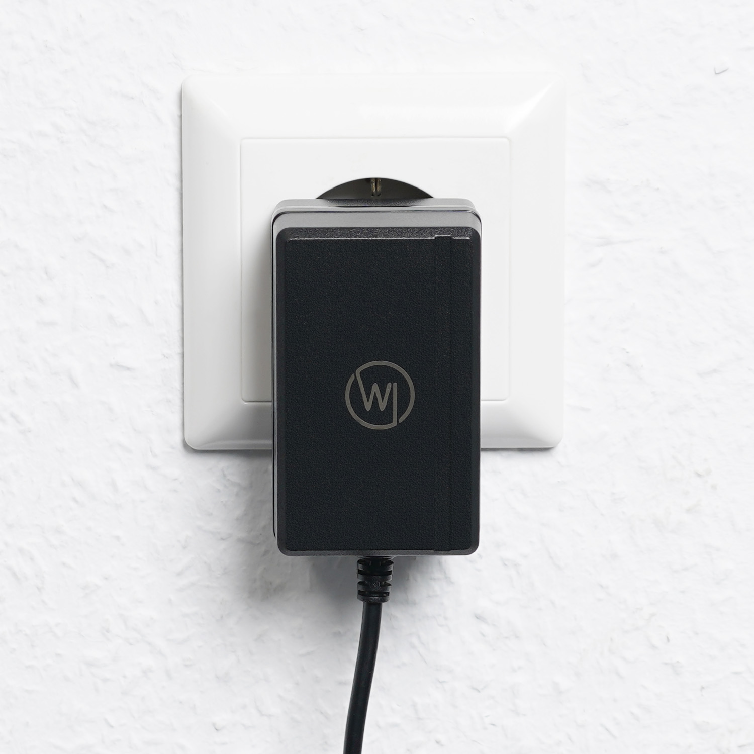 Schwarzes Netzteil, das in eine weiße Steckdose gesteckt ist. Der Adapter hat ein Logo.